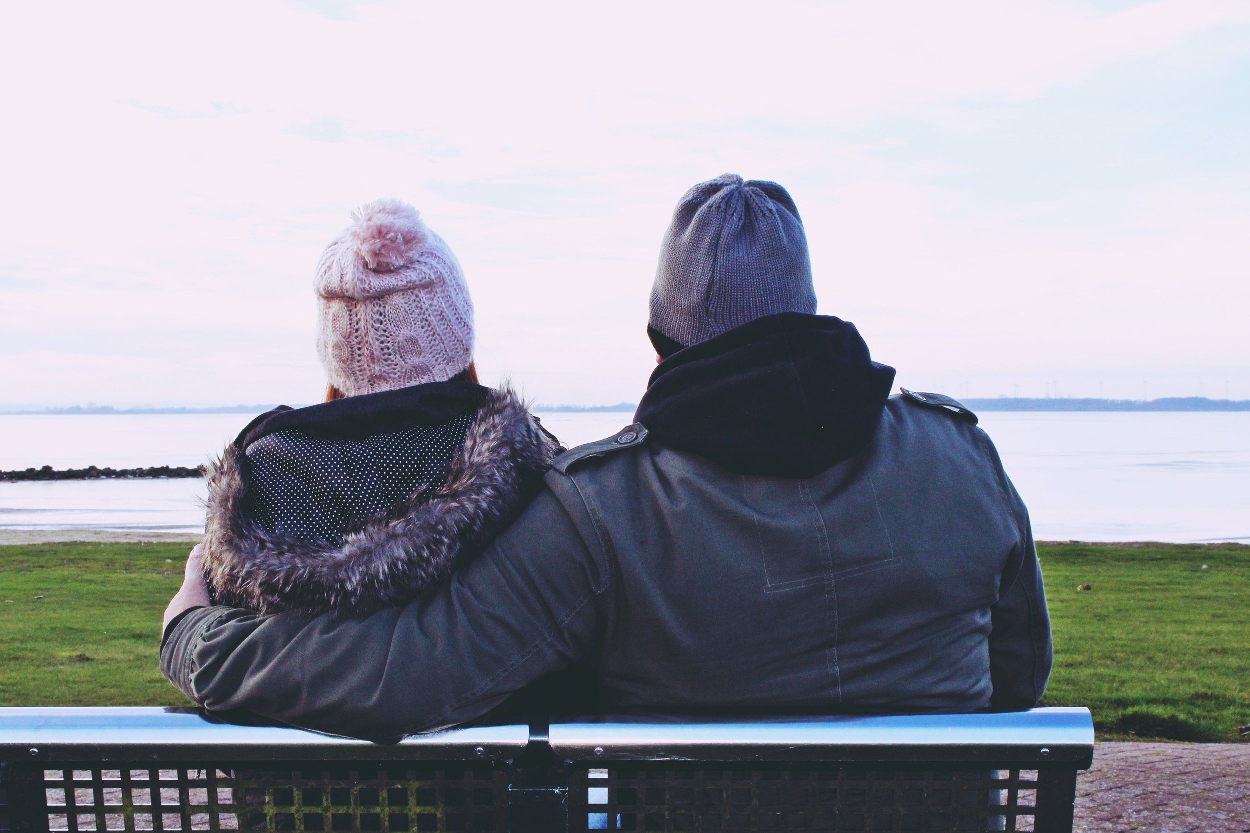 Two partners sitting together on a bench, one with his arm around the other, representing connection and support through marriage counseling in Worcester.