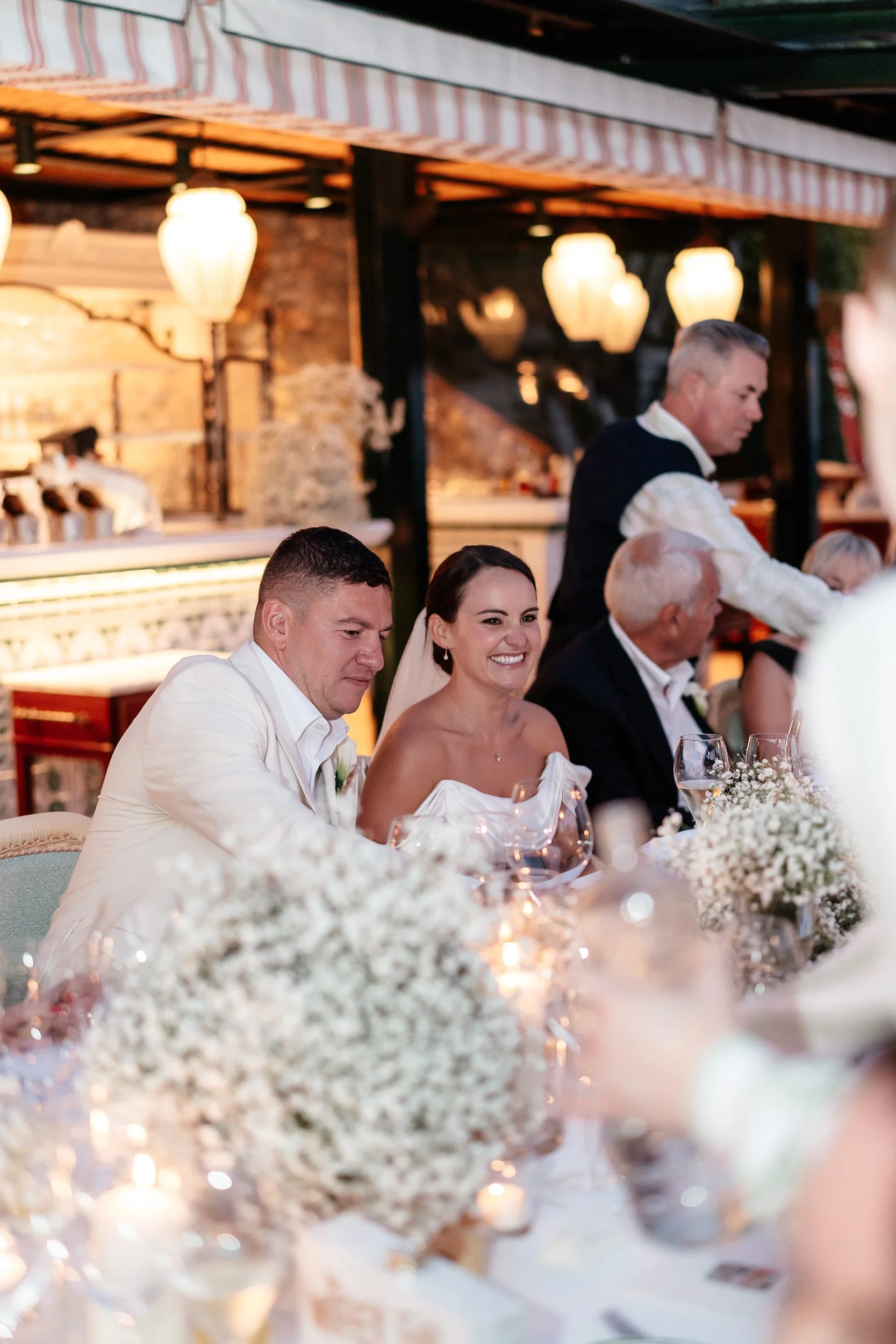 Bride and groom sitting at a wedding reception table in warmly lit rustic venue Belmond Splendido Wedding, Portofino Italy. Photos taken by editorial destination wedding photographer Weddings by Emma Olivia. 