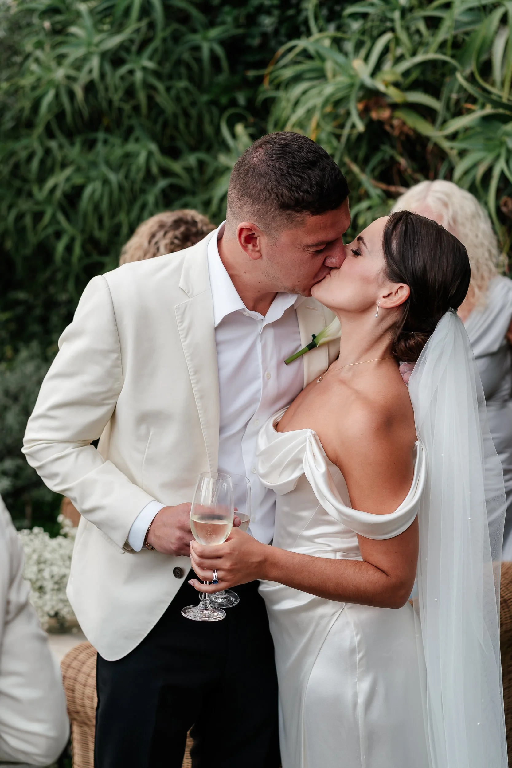 A newlywed couple sharing a kiss during their wedding ceremony, with the bride holding a glass of champagne overlooking Portofino at a Belmond Splendido Wedding, Portofino Italy. Photos taken by editorial destination wedding photographer Weddings by 
