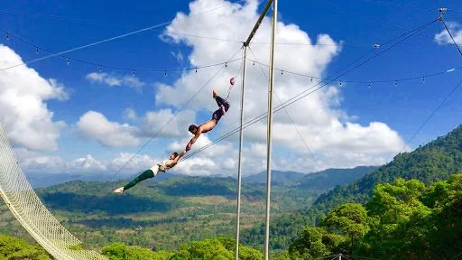 A person performing acrobat on a high wire outdoors with a scenic mountain and green landscape background.