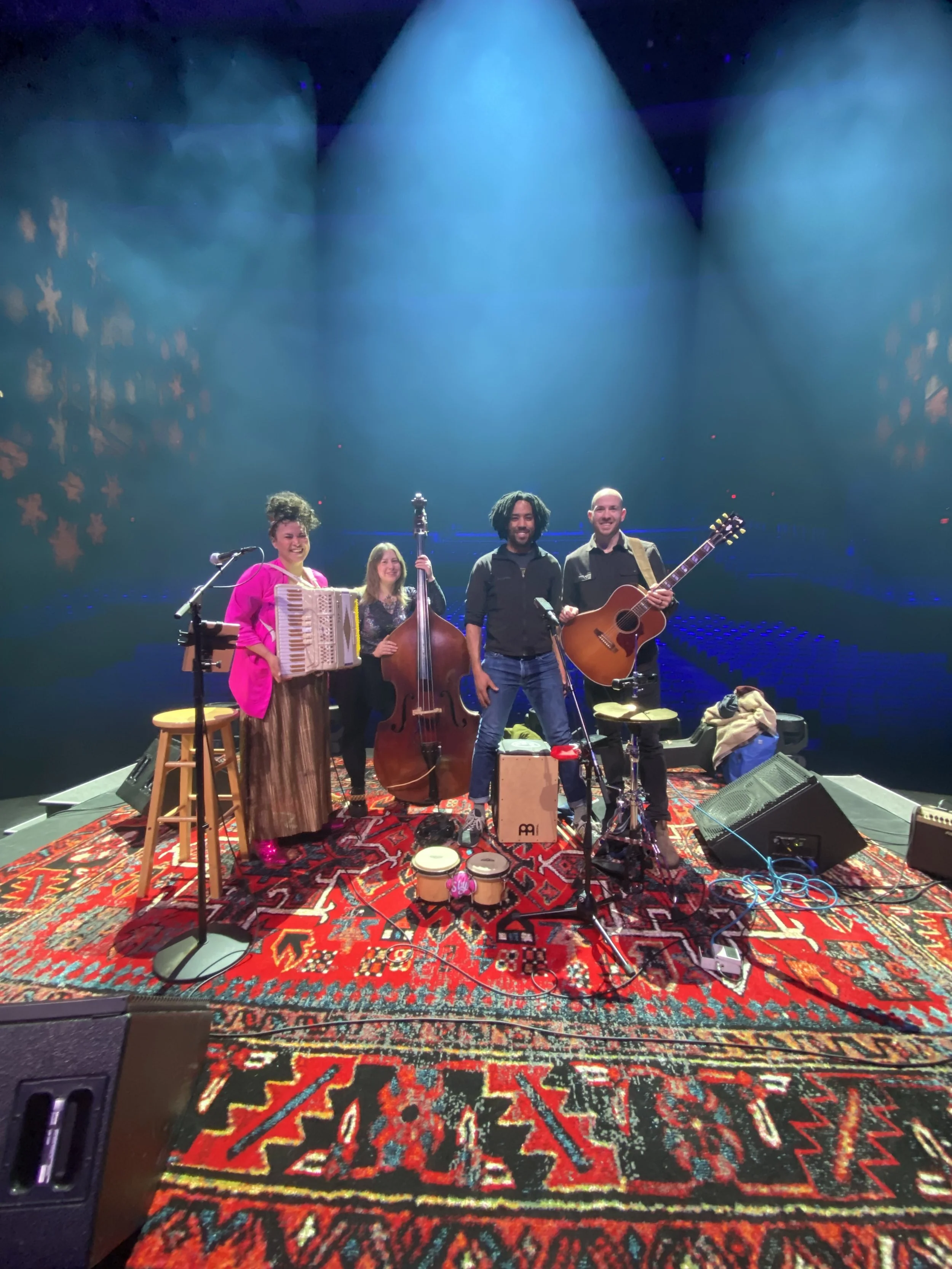 Tiff Hall and her coverband Goldtooth pose with their acoustic instruments on the Jubilee Auditorium stage, with moody blue lights in the background.