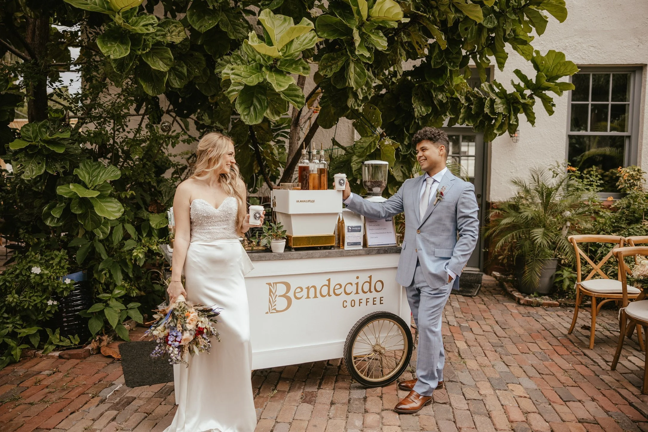 Bride and groom posing beside a Bendecido Coffee cart at an outdoor wedding