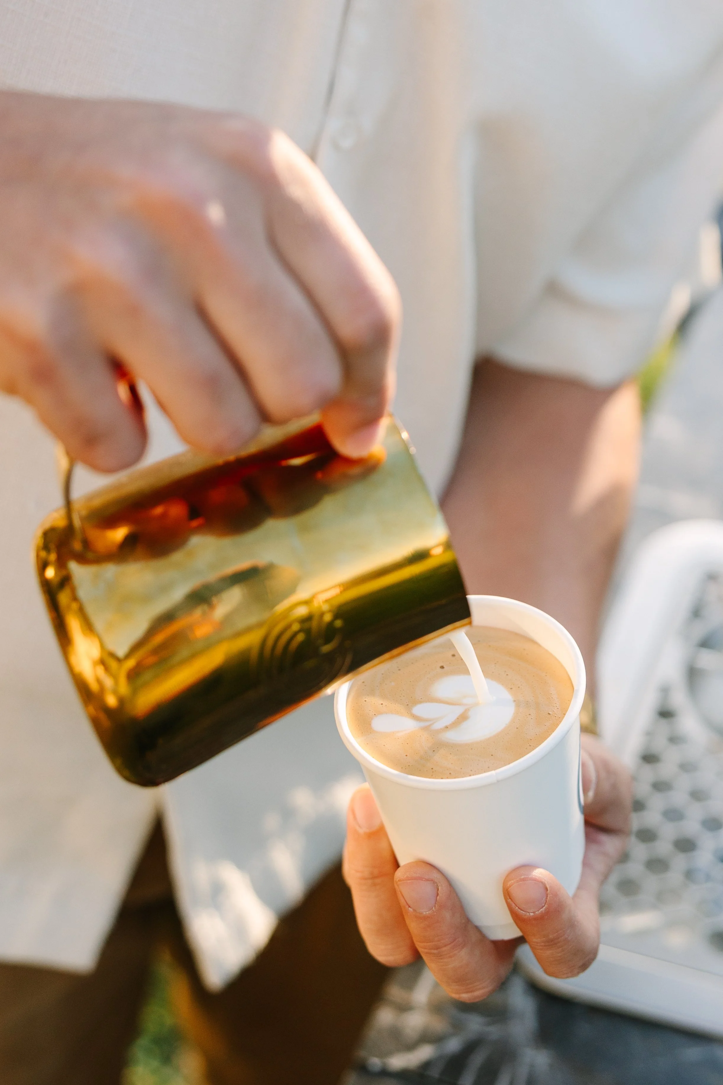Person pouring cream into a cup of coffee with latte art.