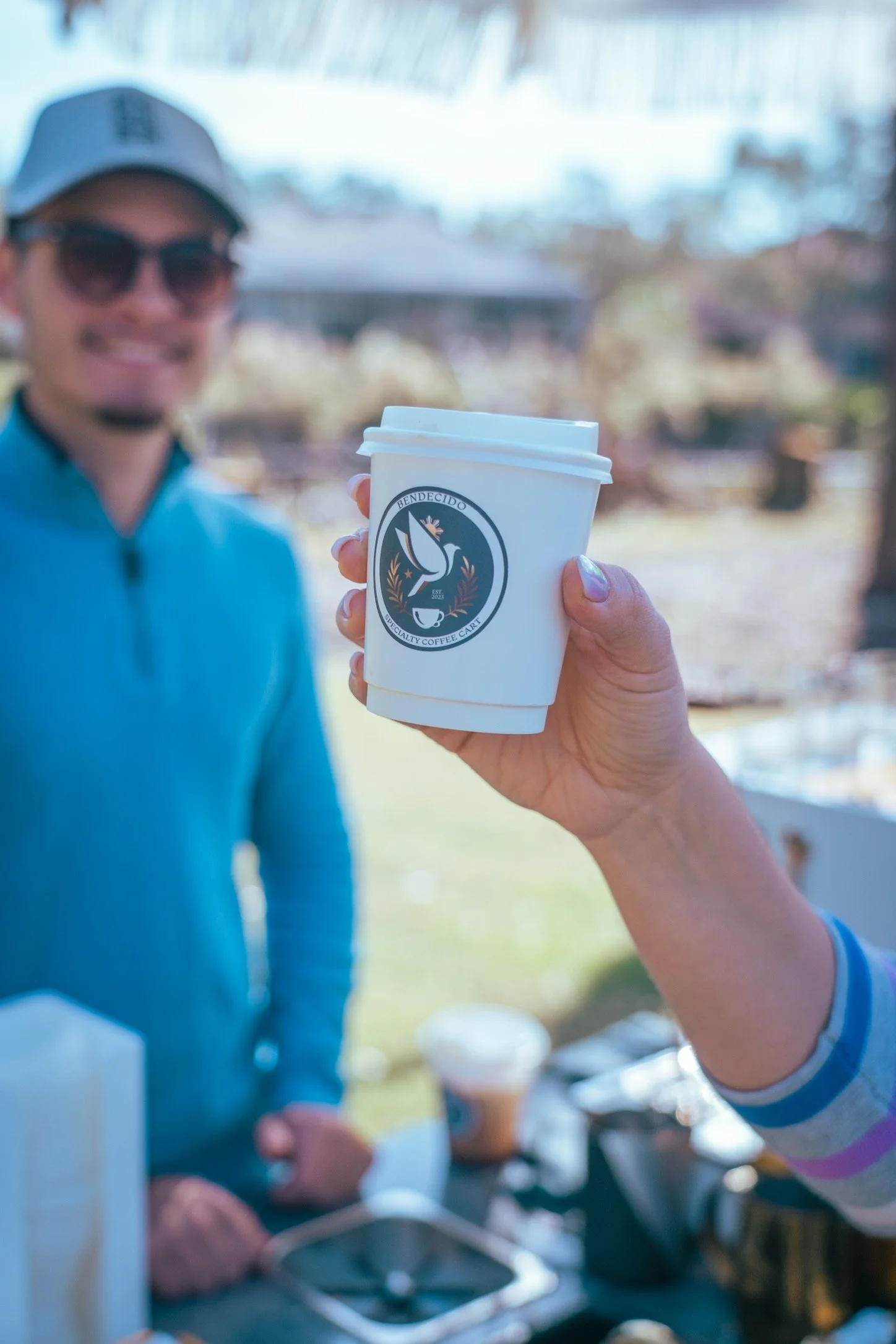 Smiling guest in a blue shirt holding a Bendecido Coffee cup beside the coffee cart