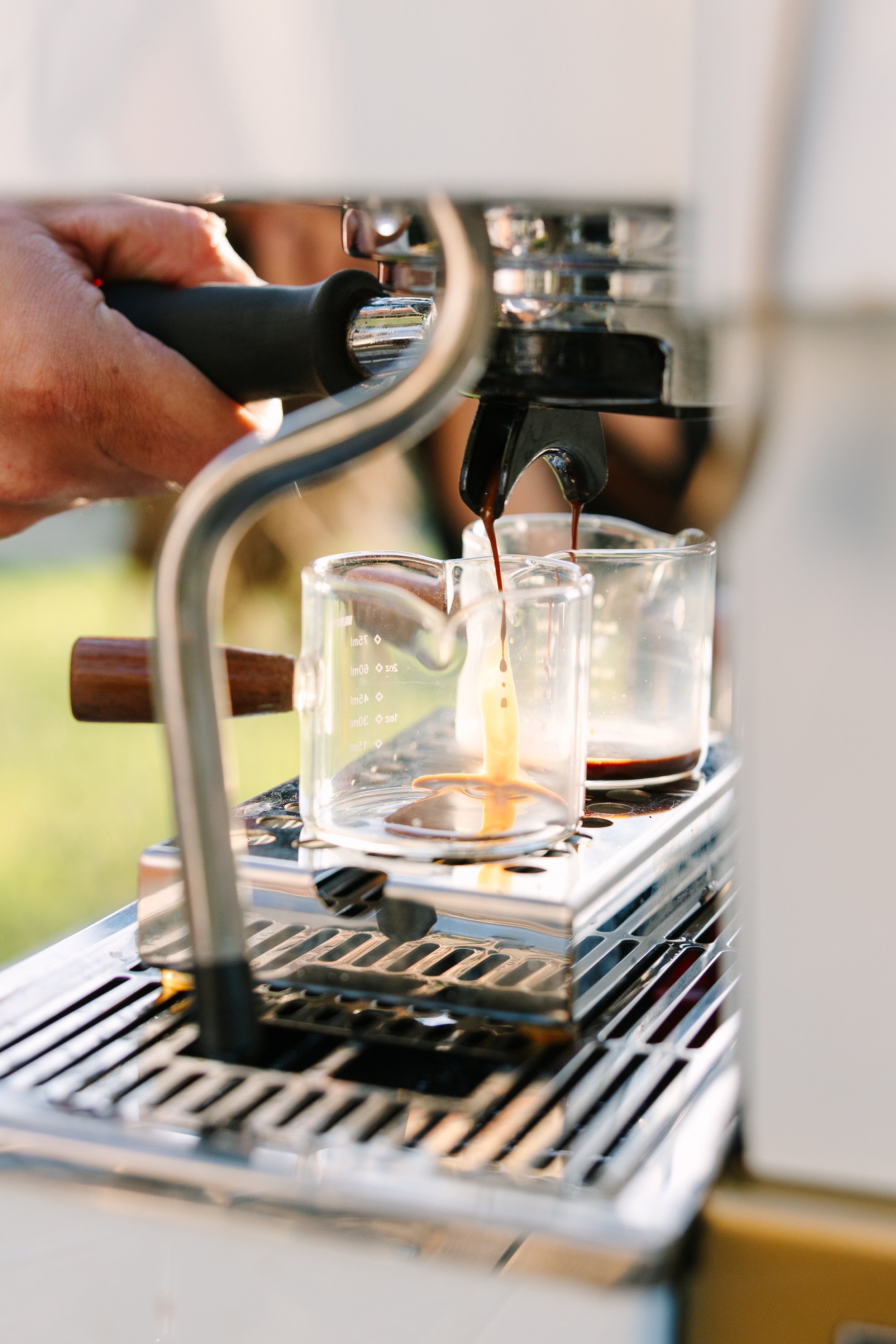 Close-up of a person operating an espresso machine, pouring brewed espresso into two small glass cups.
