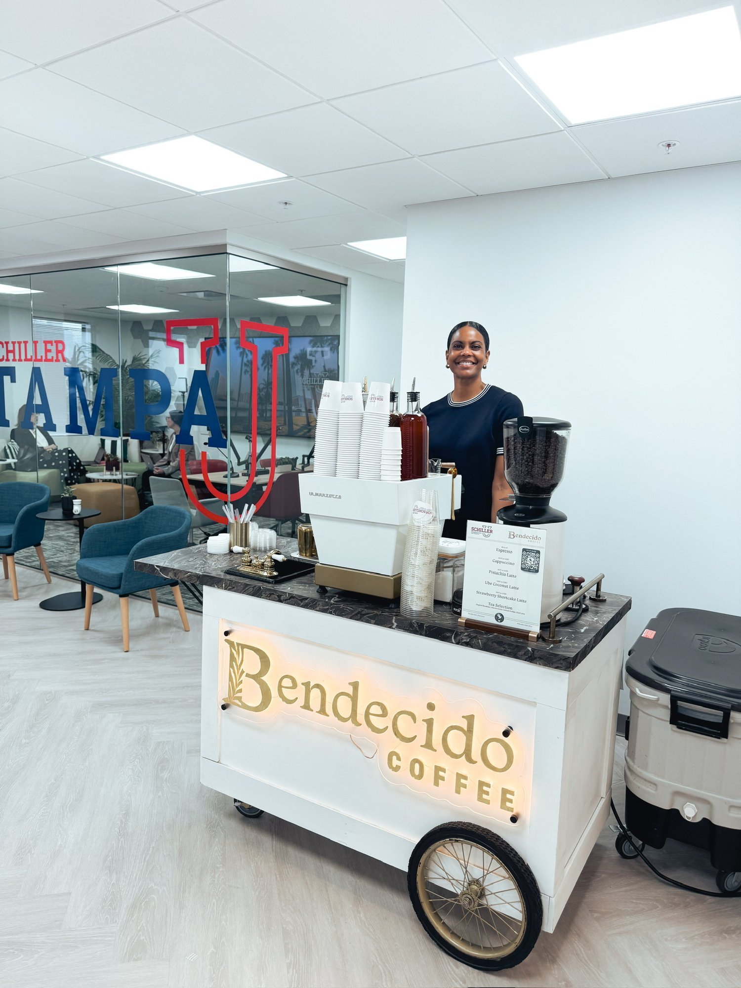 Smiling barista serving from the Bendecido Coffee espresso cart in a Tampa corporate office lobby