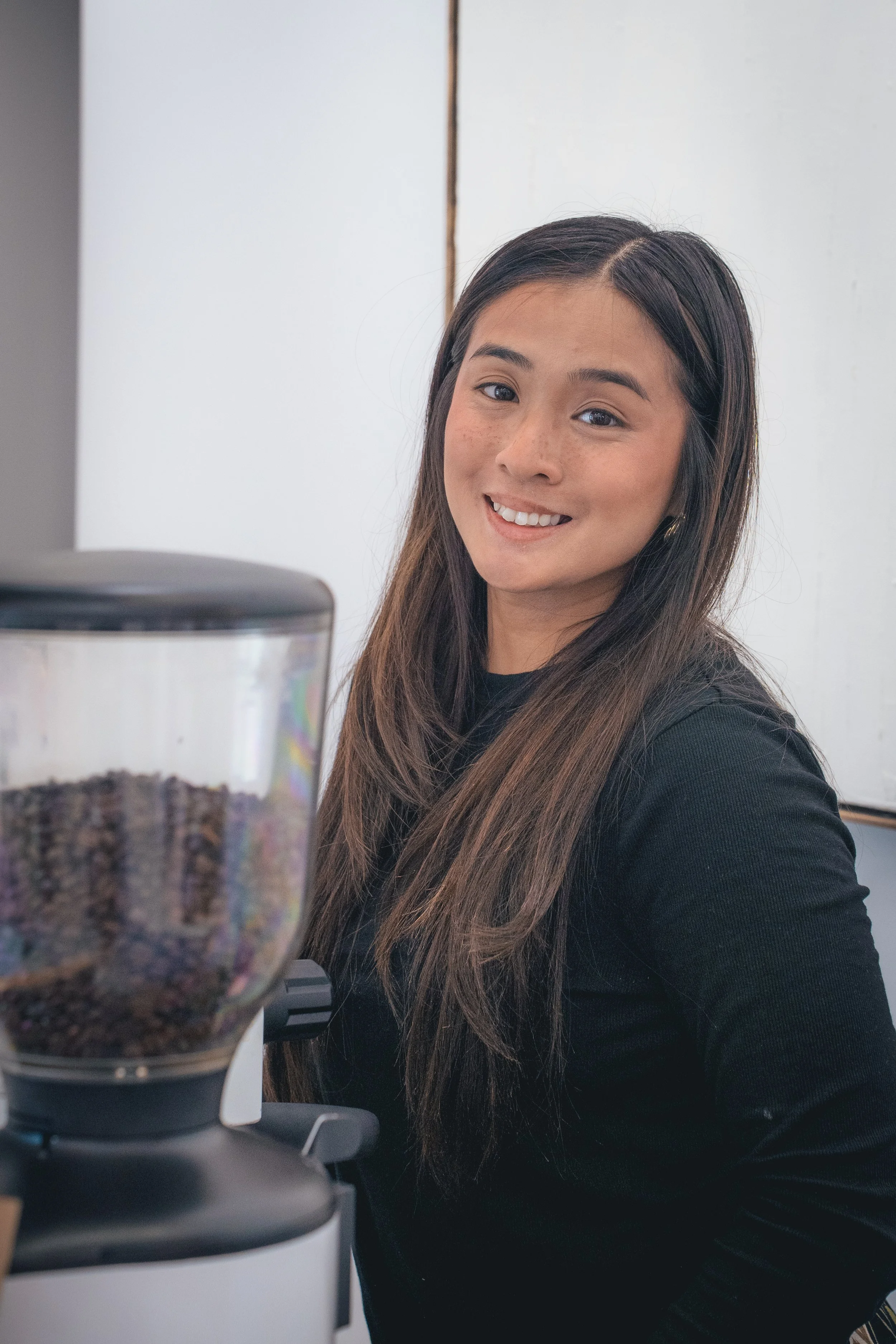 Smiling Bendecido team member next to a coffee grinder