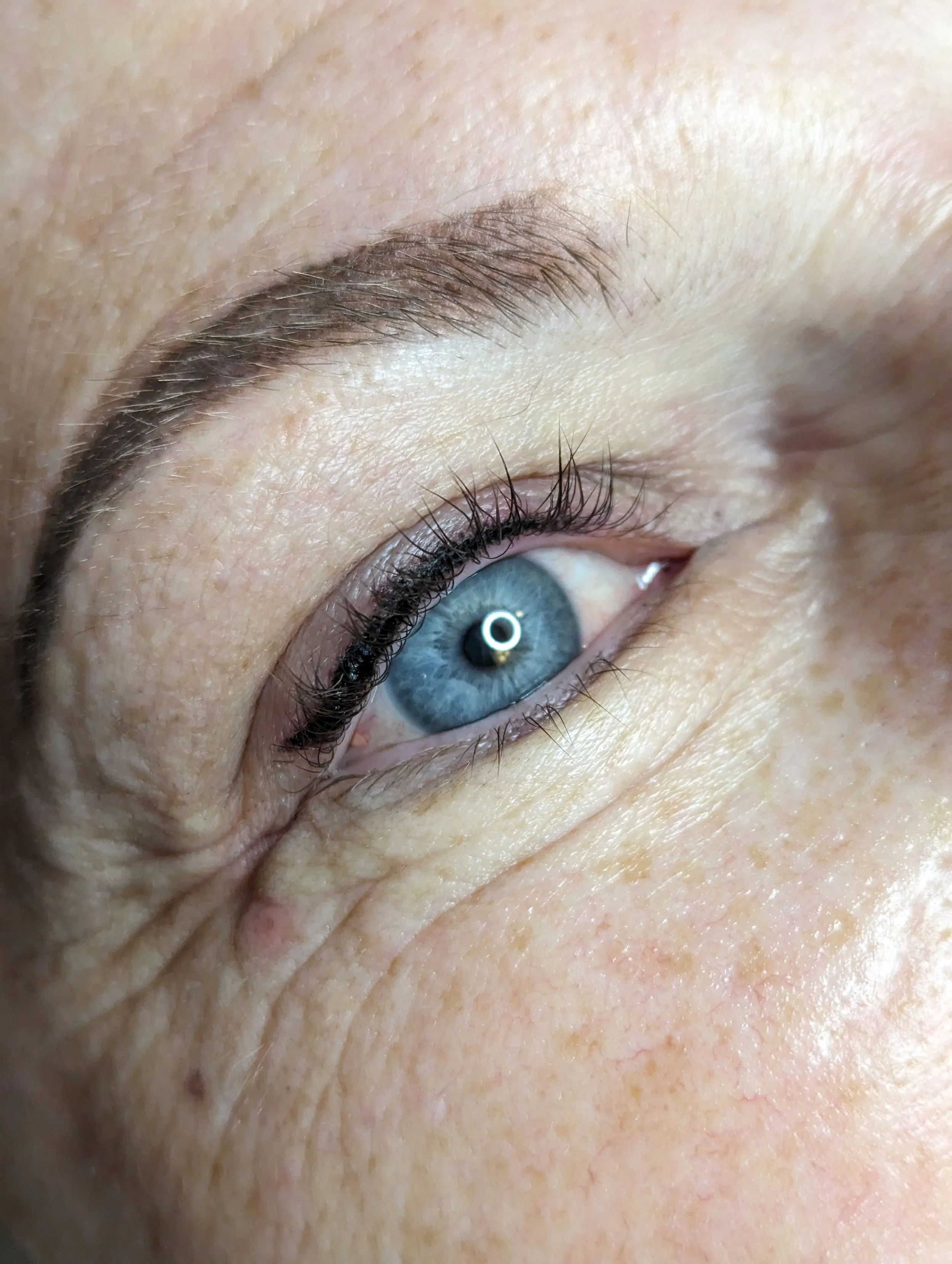Close-up of a human eye with blue iris, black eyelashes, and an eyebrow, showing skin details and natural texture.