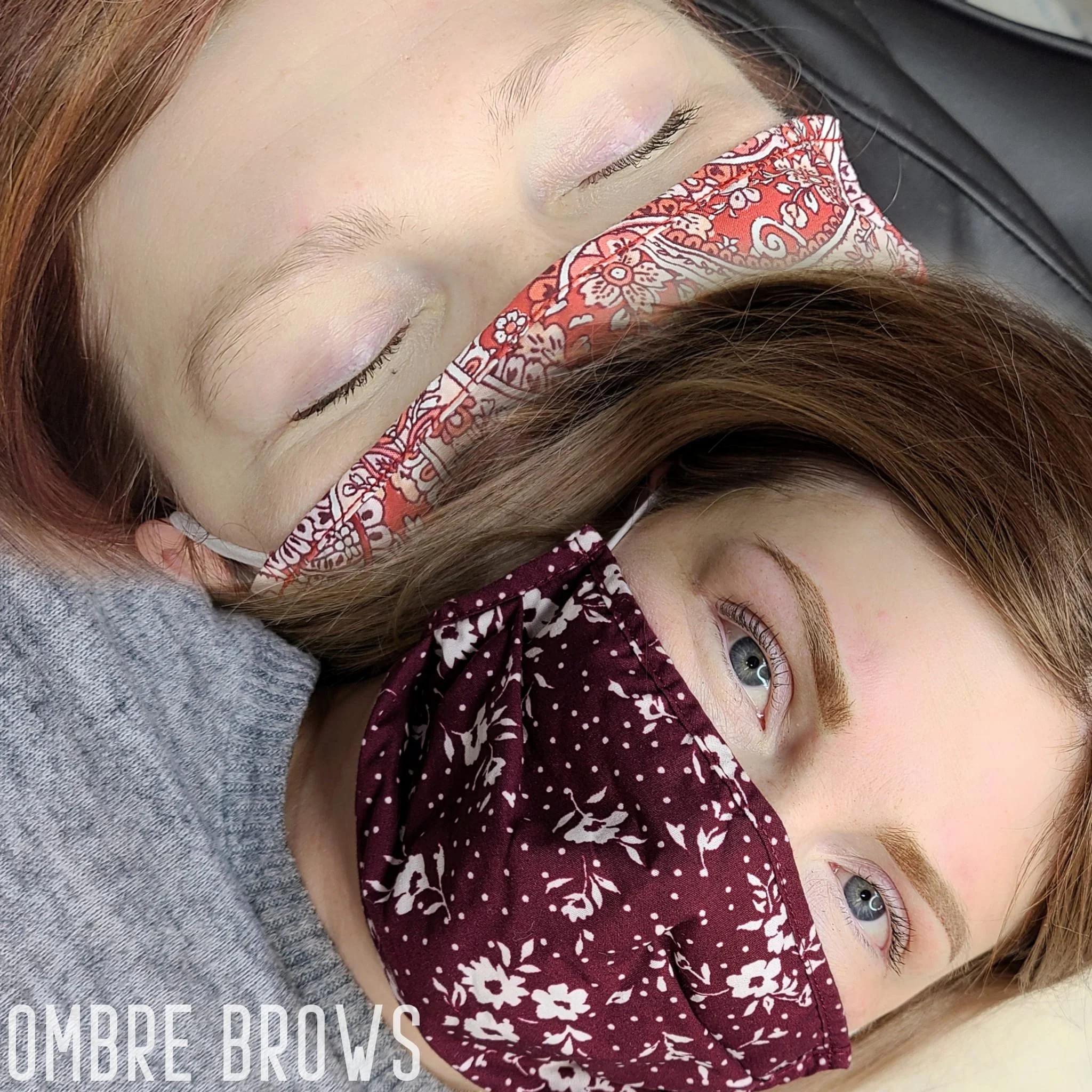 Two women lying down, one with closed eyes and a patterned face mask, the other with open blue eyes and a different patterned face mask.