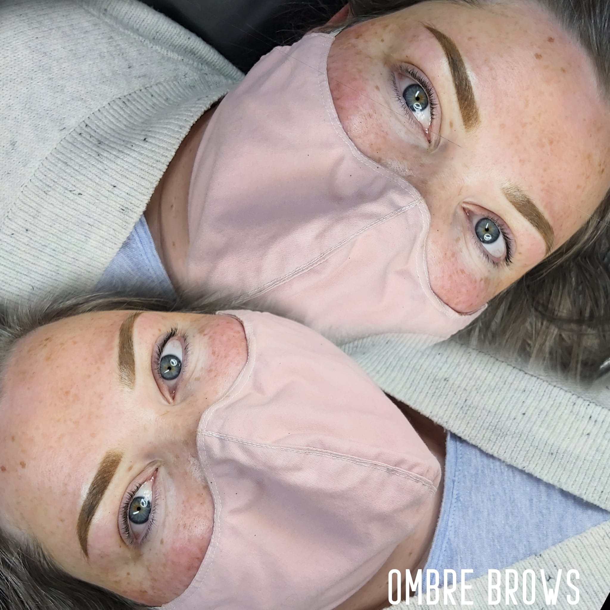 A woman with blue eyes, freckles, and well-defined eyebrows wearing a light pink face mask covering her nose and mouth, lying down with her head resting on a surface.