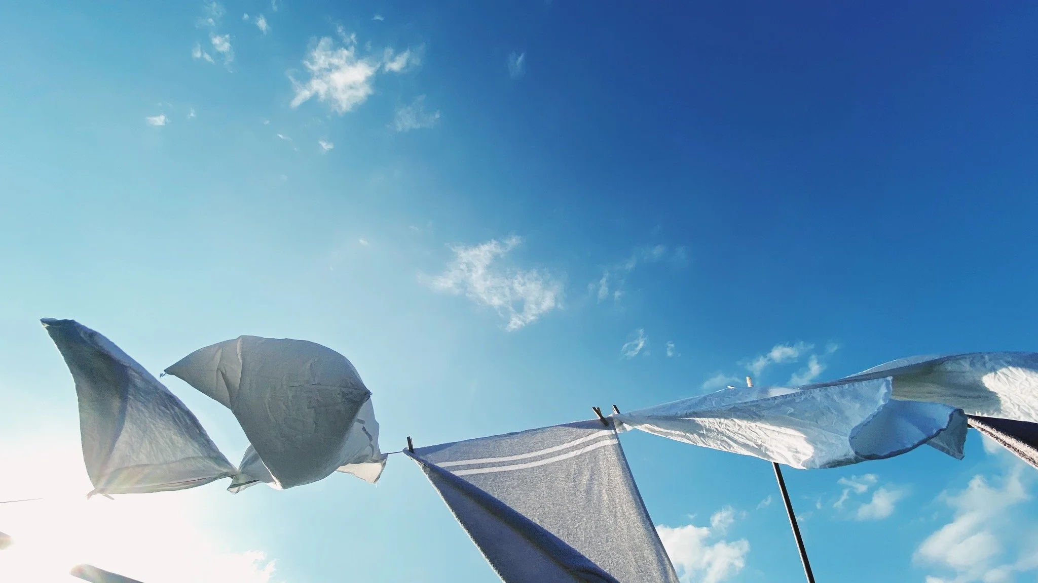 Clothes hanging on a clothesline outdoors under a blue sky with scattered clouds.