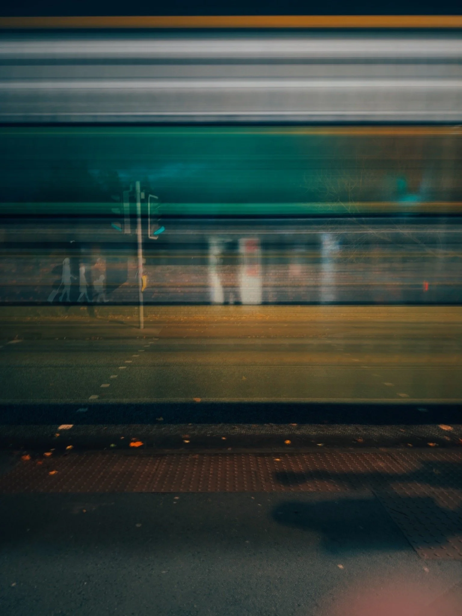 Blurred city street scene with silhouettes of pedestrians walking, traffic signals, and railroad tracks.