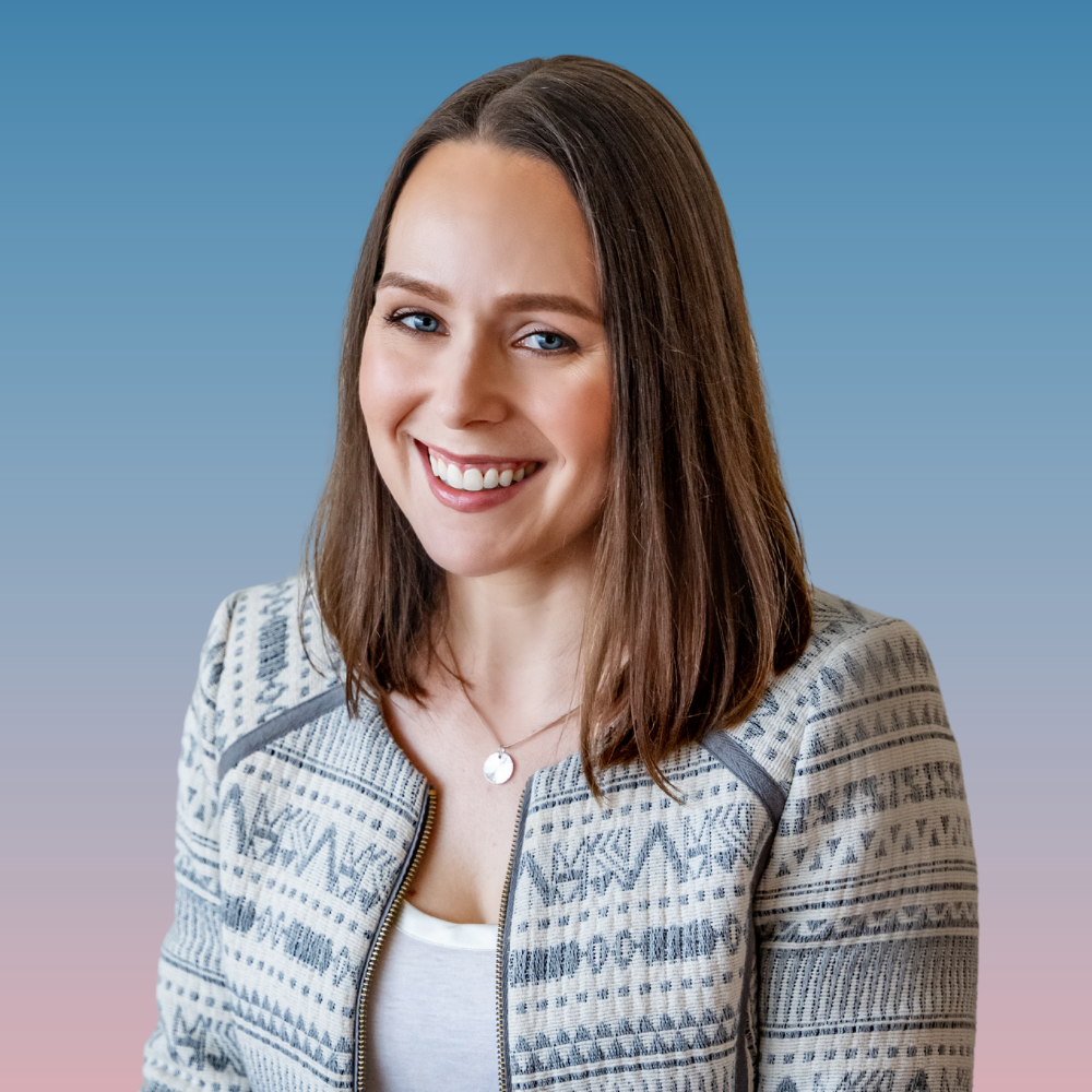 A smiling woman with shoulder-length brown hair, blue eyes, wearing a white blouse and a thin black choker necklace, standing in front of abstract blue and green paintings on a white wall.
