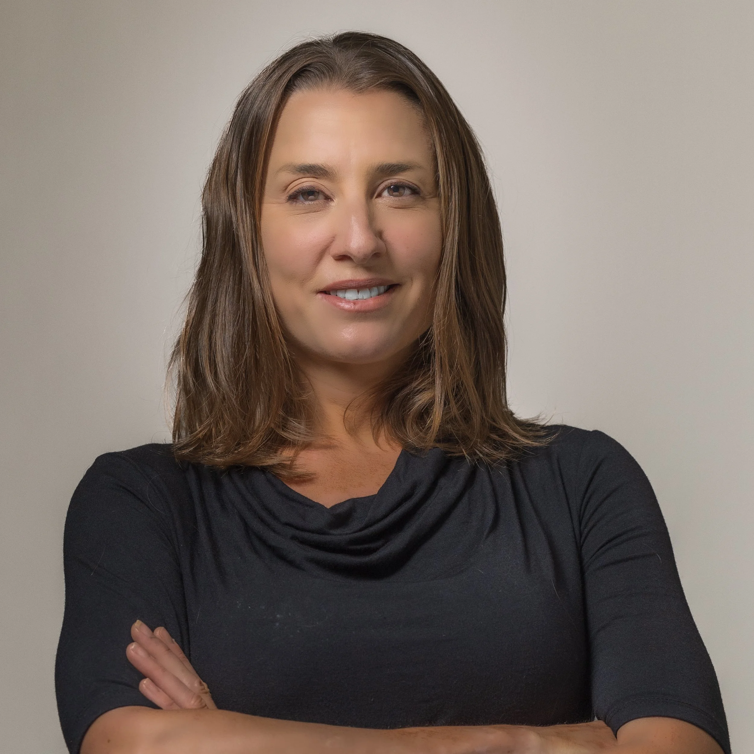 Smiling woman with brown hair wearing a black top, arms crossed, standing against a neutral background.