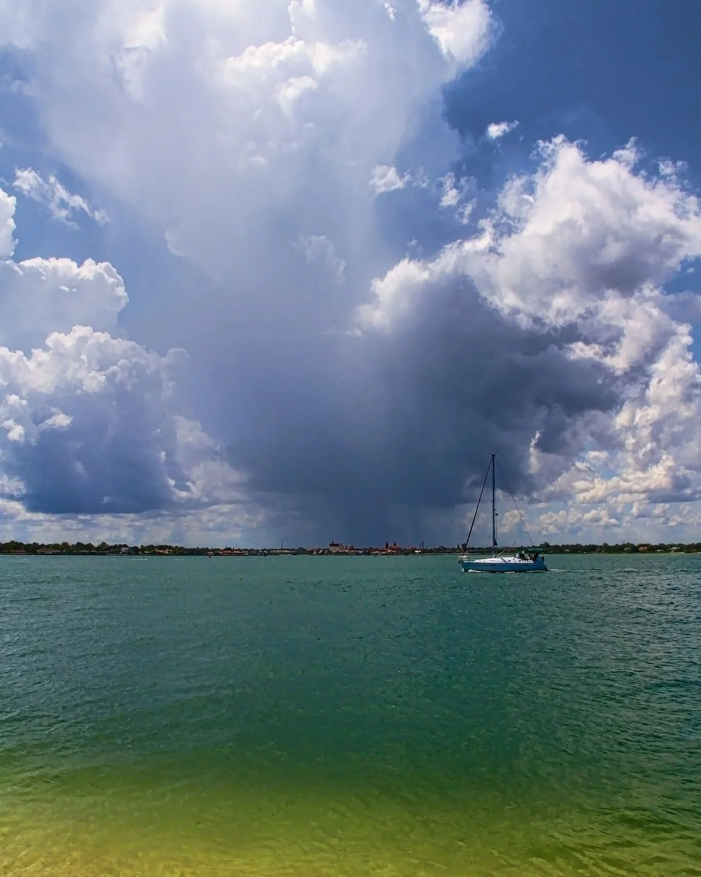 A sailboat on a calm body of water with a cloudy sky and distant shoreline.