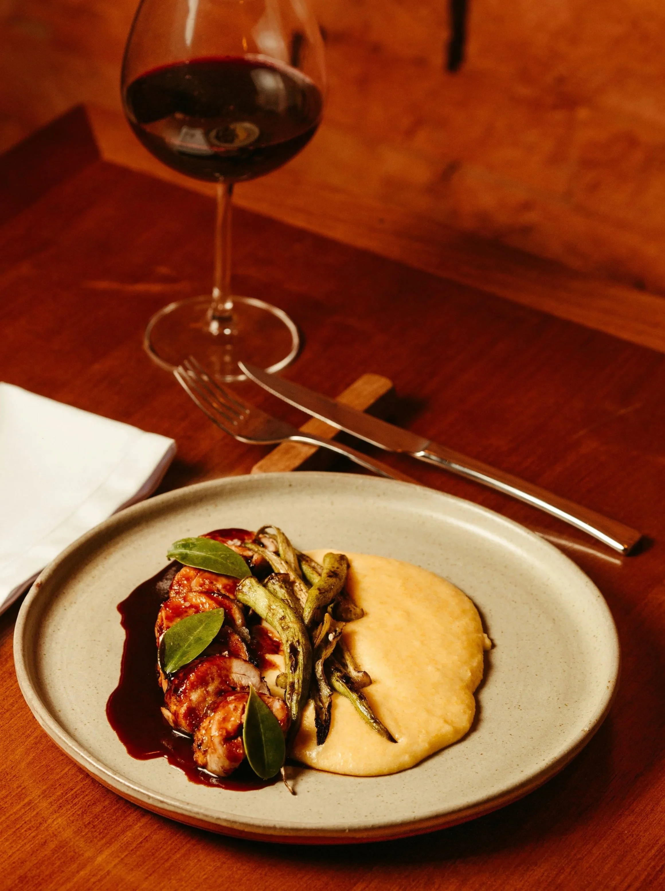 A plate of roasted vegetables, mashed potatoes, and a small salad with leafy greens, served on a ceramic plate. A glass of red wine is on a wooden table in the background.