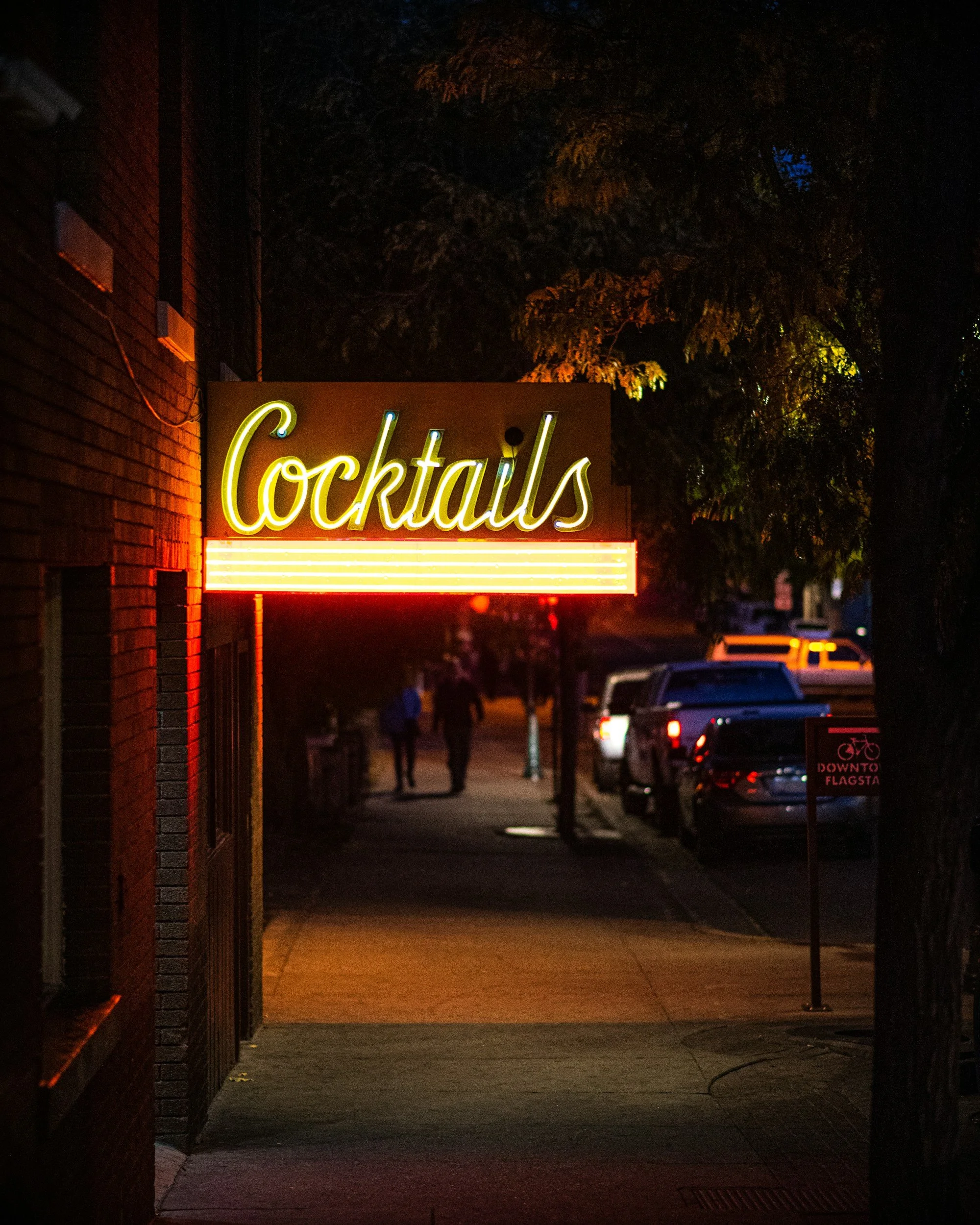 Neon sign reading 'Cocktails' on a dark street at night.