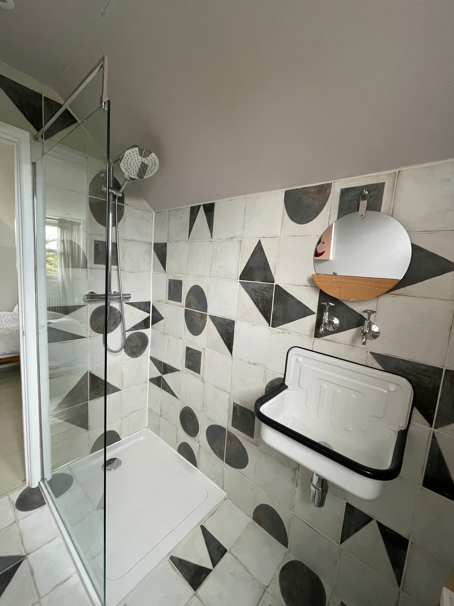 Bathroom with a glass shower enclosure, black and white patterned tiles, a small round mirror, and a white heater