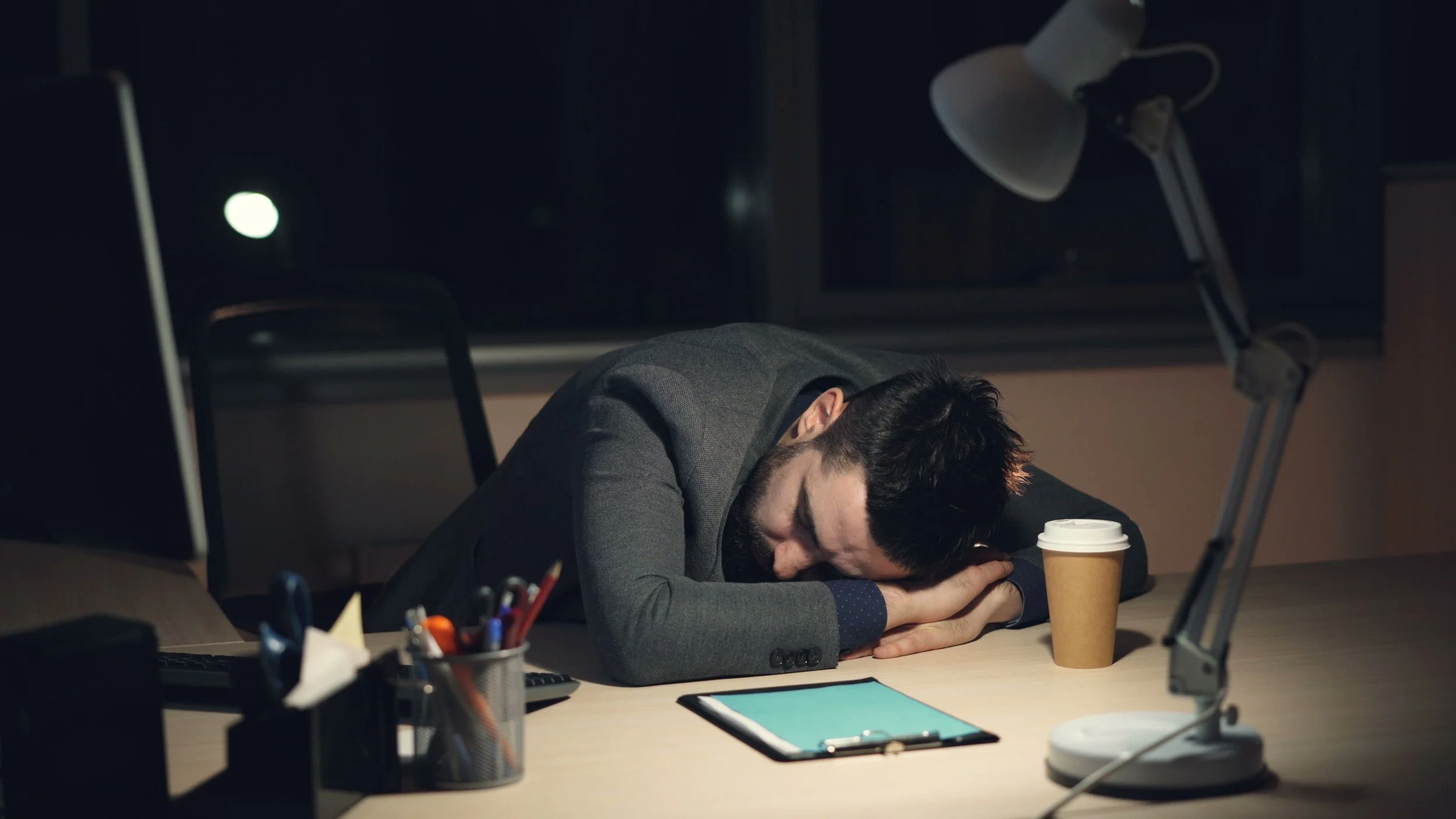 A man sleeping at his desk with his head on his arms.