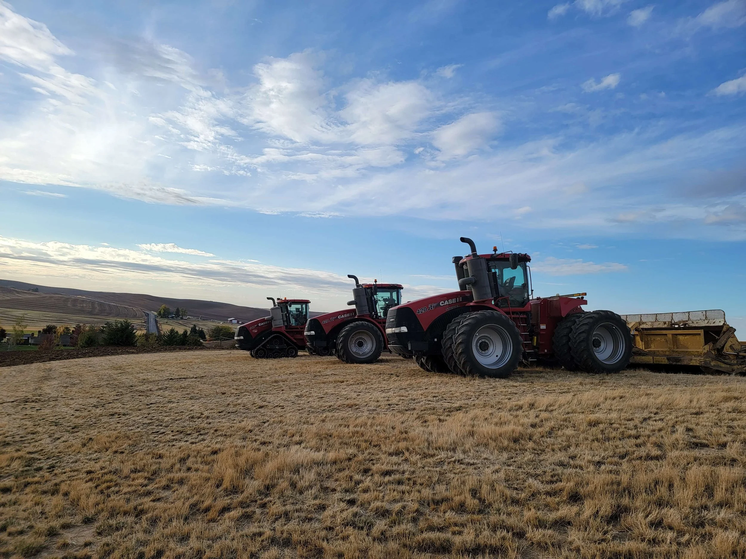 Three red EXCO tractors lined up on a field with rolling hills behind them.