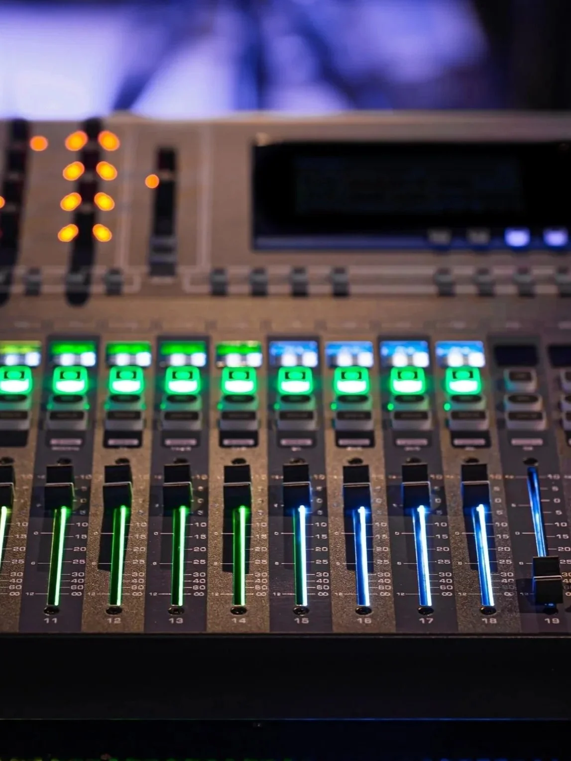 A professional audio mixing console with illuminated faders, knobs, and buttons, used for sound control in a studio or live event.