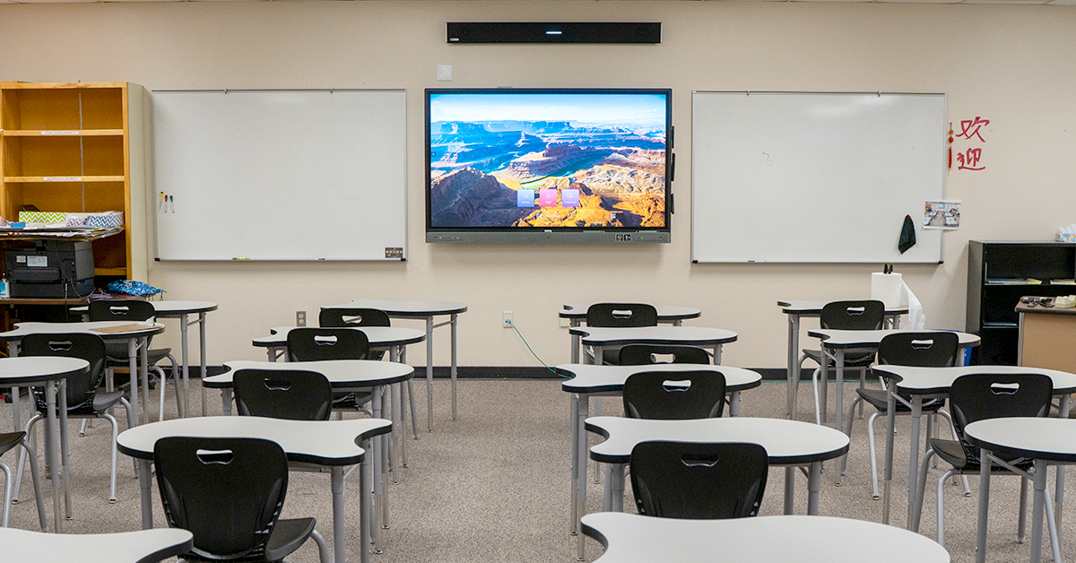Modern classroom space featuring white desks and black chairs, paired with a large digital display and commercial whiteboards, integrating premium office furniture, smart technology, and advanced AV infrastructure tailored for modern workplaces.