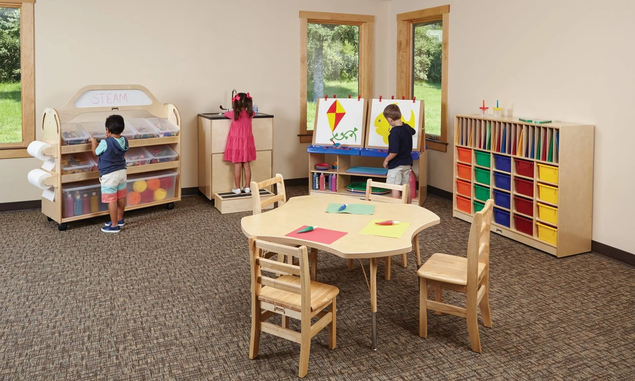 An Oxilium PreK and early learning classroom layout featuring play-based sensory light tables, ergonomic toddler wobble stools, a mobile reading nook pod, tactile wall panels, and an interactive edtech display for early childhood development.
