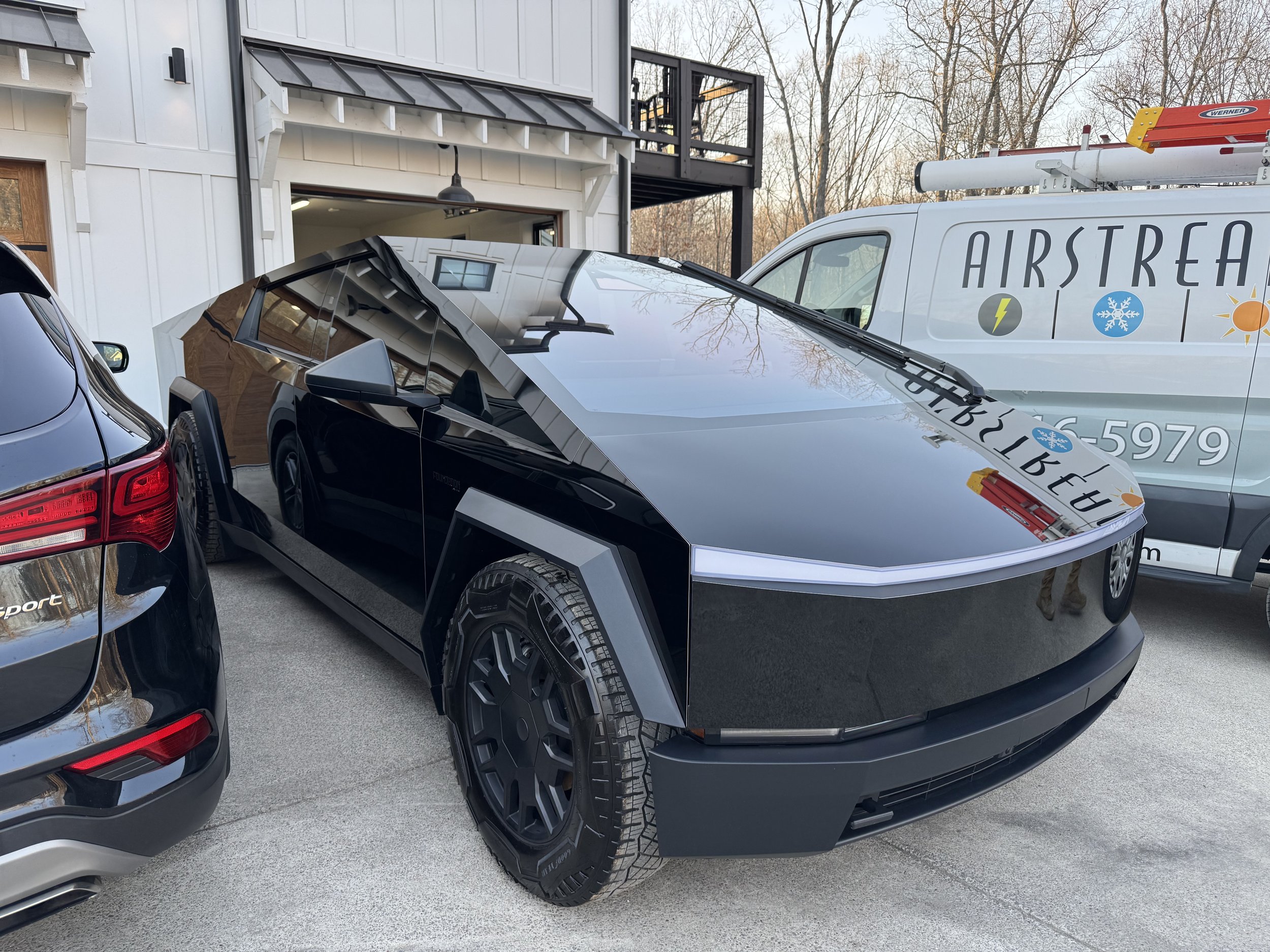 Black and silver sporty electric vehicle parked between a black SUV and Airstream trailer with weather icons and phone number.