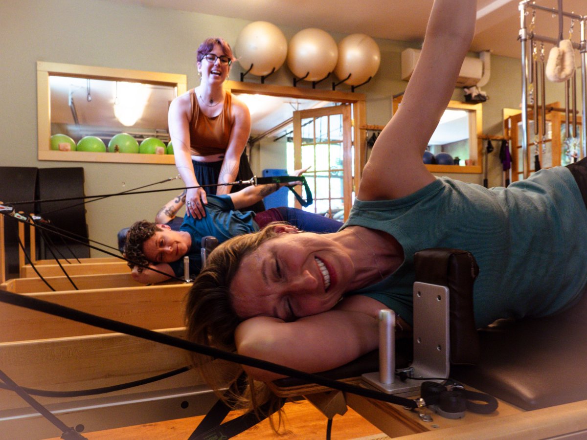 People exercising on a Pilates reformer machine in a pilates studio, smiling and laughing.