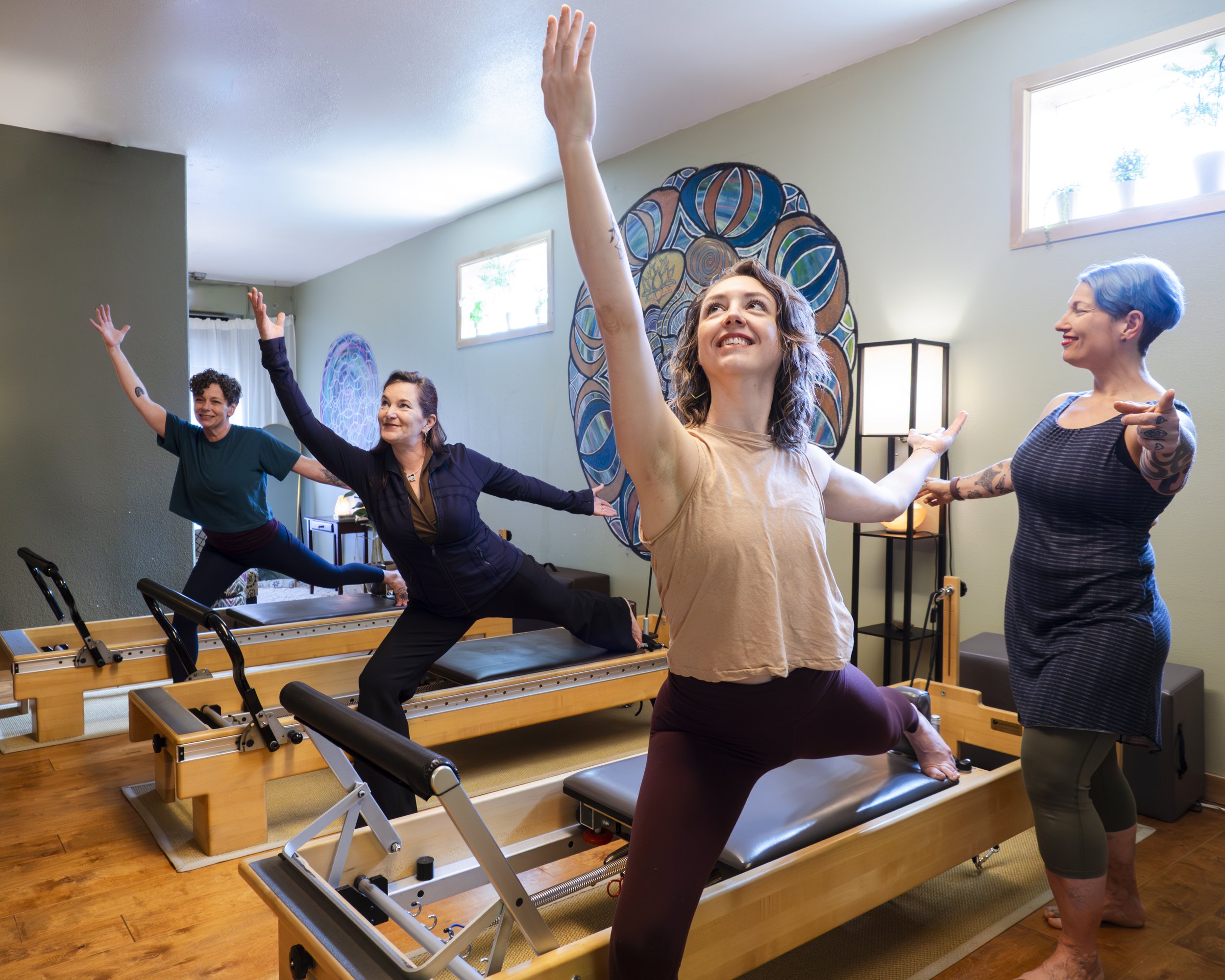 Group of women participating in a pilates reformer class in a bright room with artwork on the wall.
