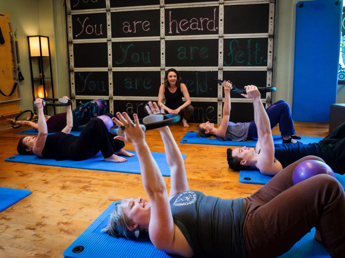 Group of people doing a Pilates mat class with Pilates mats and magic circles in a Pilates studio with motivational writing on the wall.