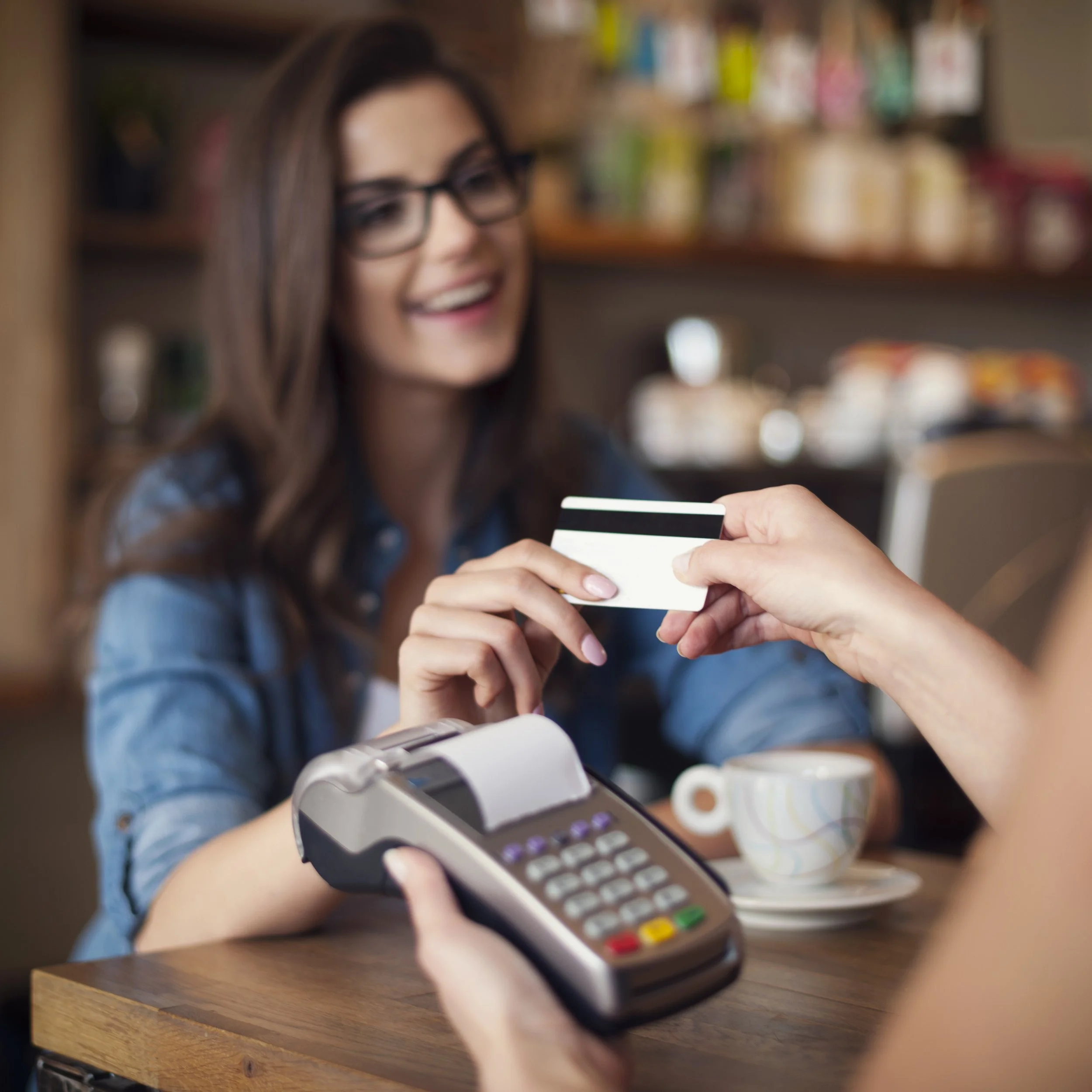 Person handing over a credit card to a cashier at a checkout counter with a card payment terminal.