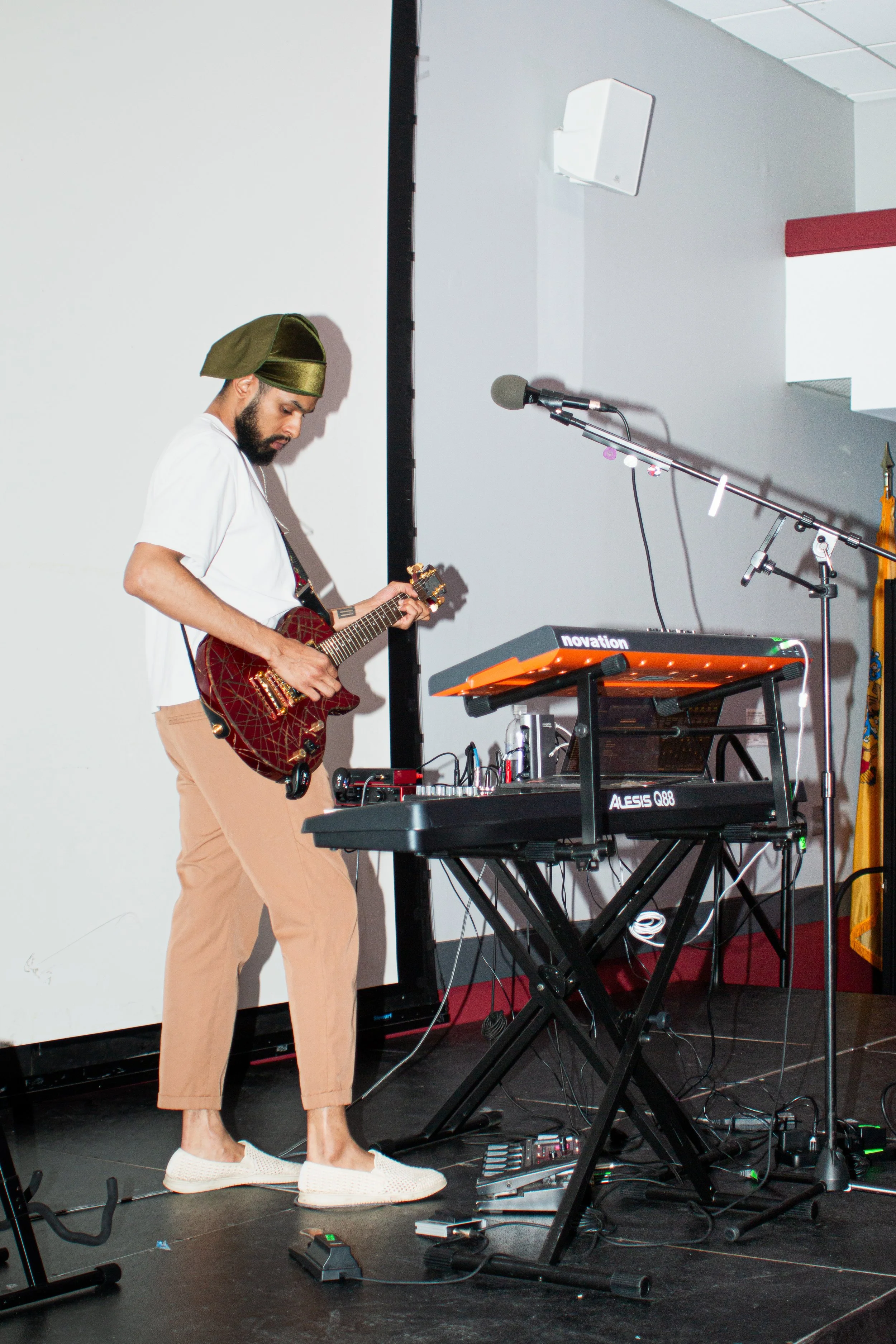 A man playing an electric guitar and standing in front of a microphone and electronic music equipment on a stage.