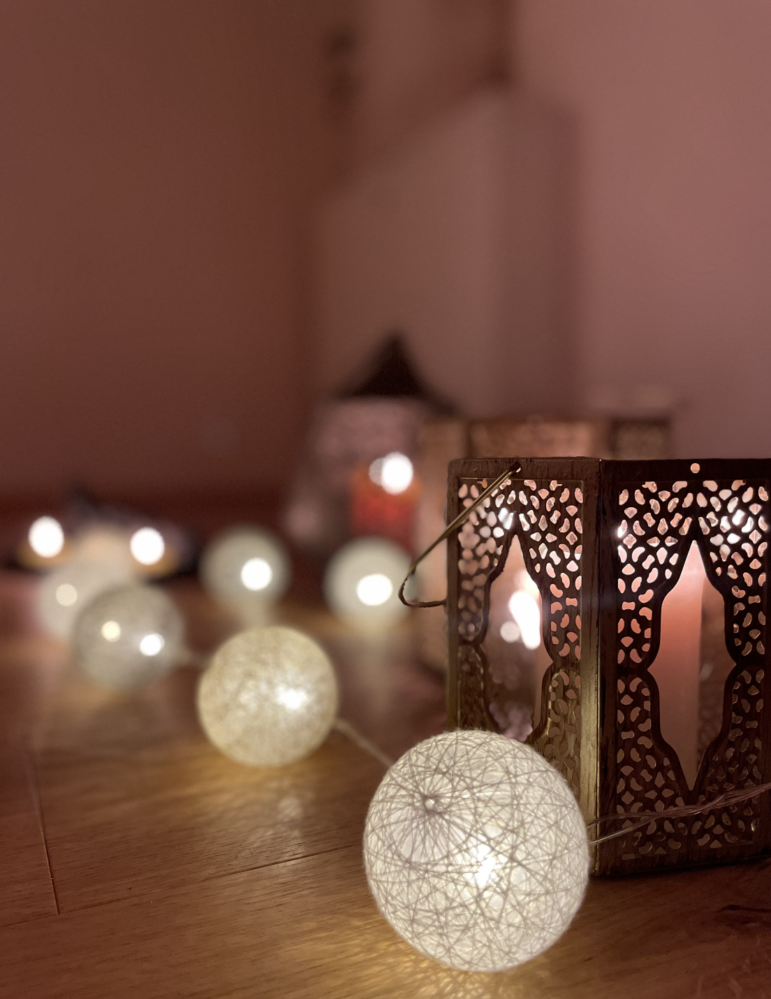 Decorative string lights with glowing spherical bulbs, a brass lantern with intricate cut-out patterns, and a blurred background on a wooden surface.