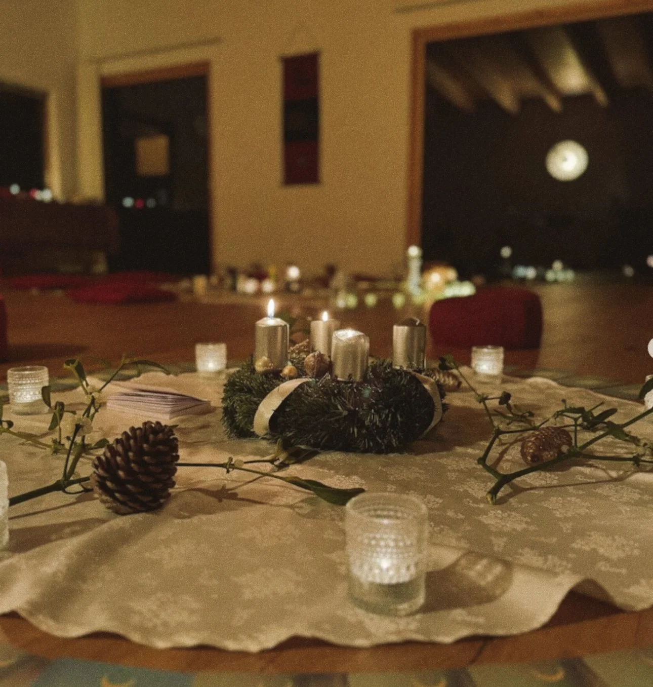 A Christmas dinner table with a centerpiece of candles, pinecones, and greenery, decorated for the holiday season, and lit candles around it.