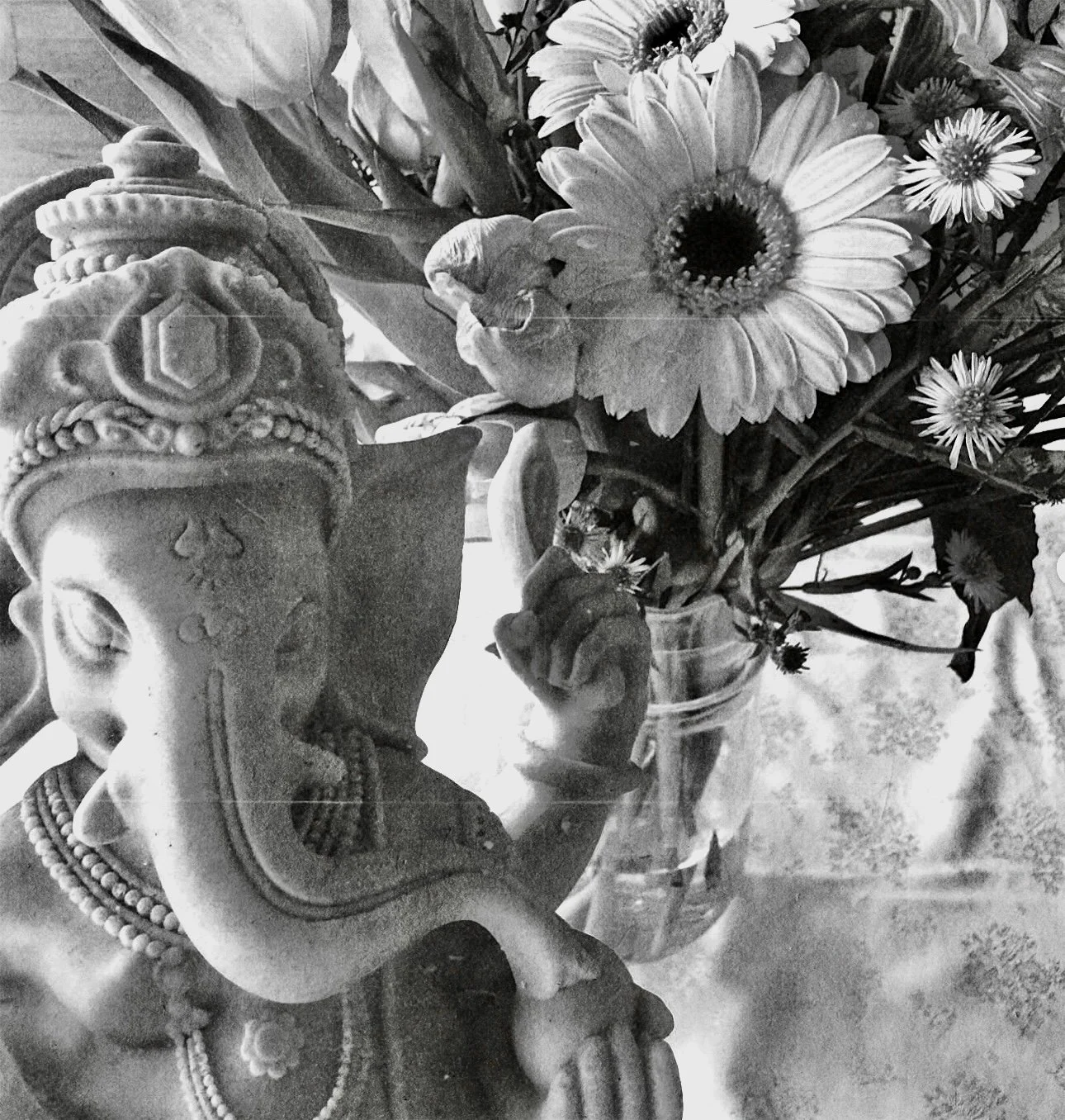 A decorative sculpture of a human face with traditional headwear and jewelry, placed next to a vase of assorted flowers including daisies.