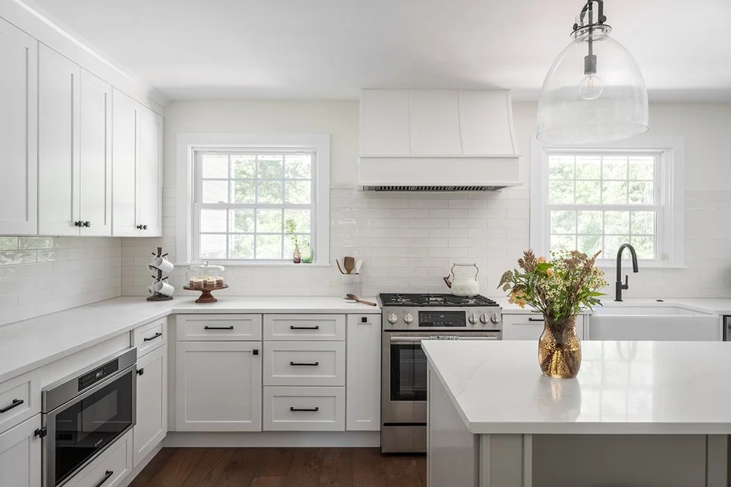 White kitchen cabinets with a white backsplash and dark wood floors. 