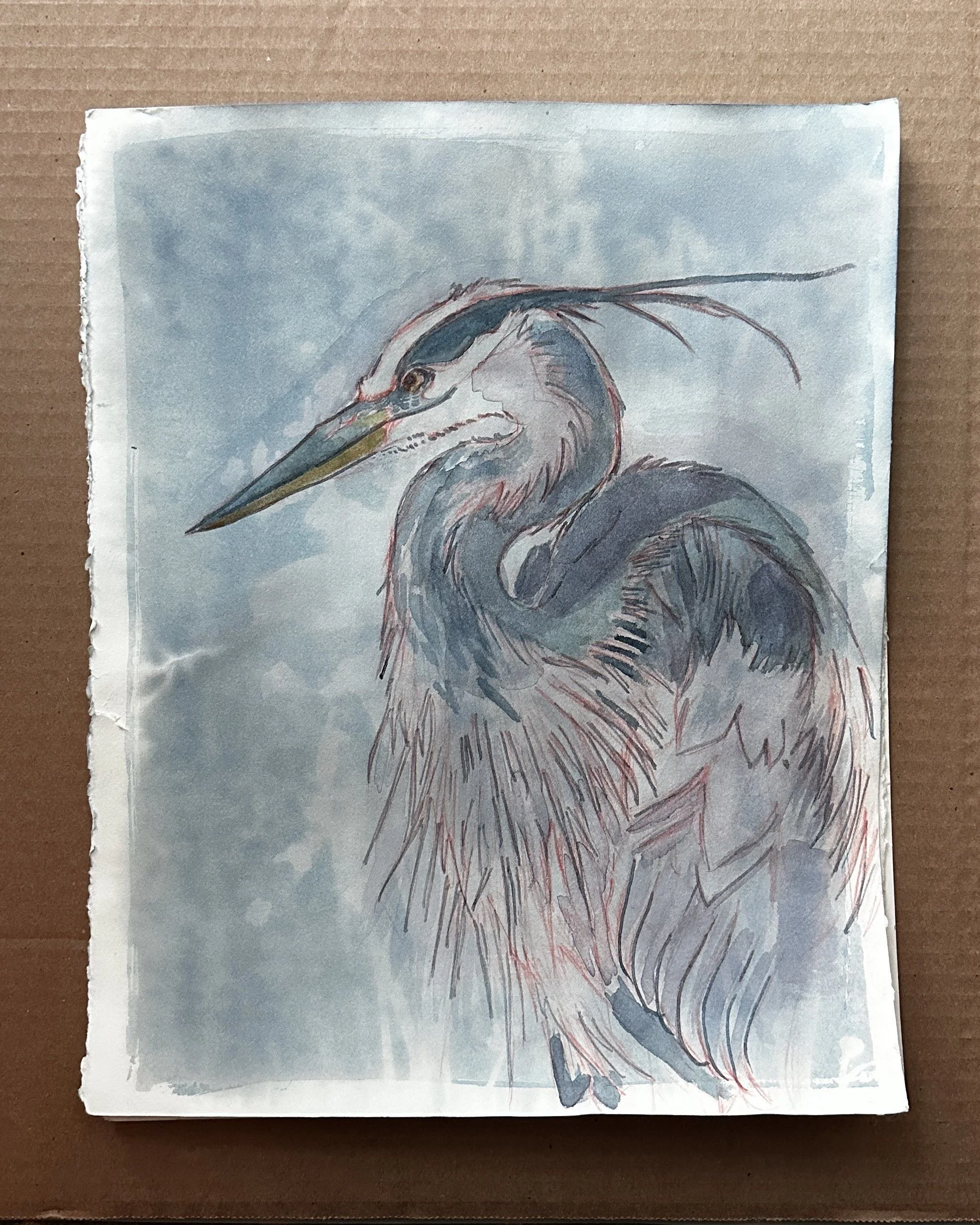 A watercolor painting of a heron with a blue sky background, on paper with torn edges, placed on a brown surface.