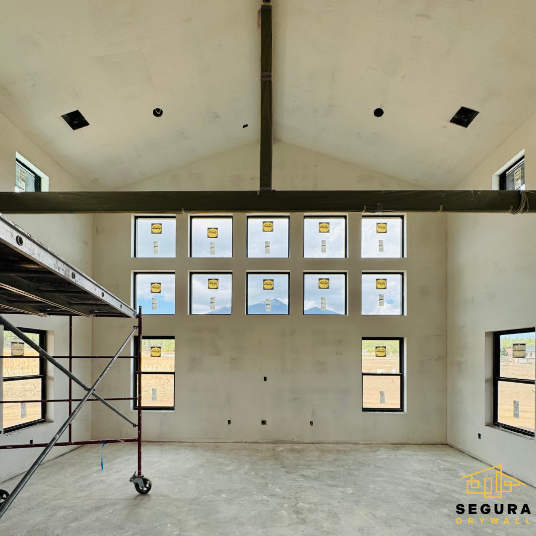 Interior of a house under construction with multiple windows, a sloped ceiling with skylights, and a scaffold on the left side.