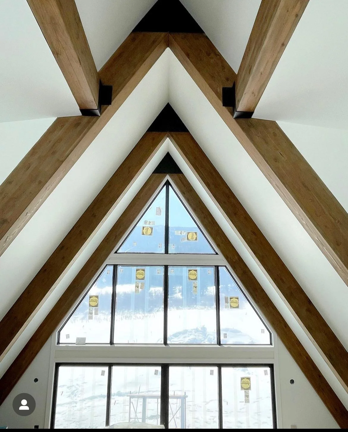 Interior view of a dormer with large triangular window, wooden beams, and snow outside.