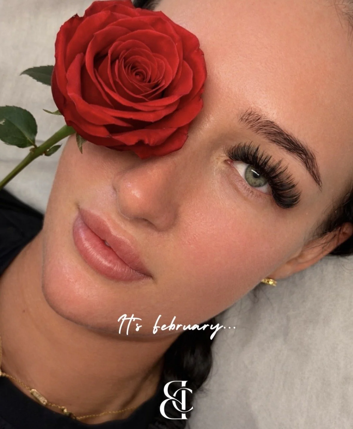 Close-up of a woman with a red rose near her eye, smiling softly, text overlay 'It's February...' and a small logo at the bottom.