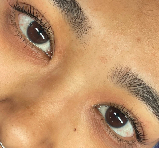 Close-up of a person's eyes and eyebrows, showing brown irises, long eyelashes, and well-groomed eyebrows.