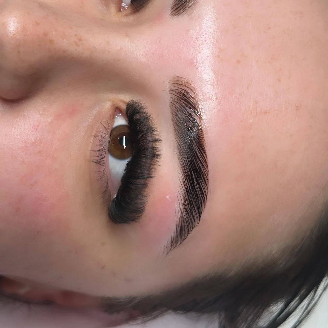 Close-up of a person's eye with long, thick, curled eyelashes and well-groomed eyebrow.