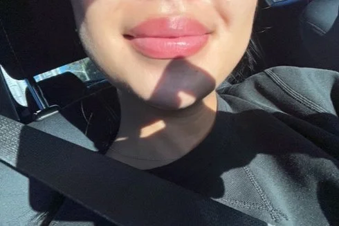 Close-up of a person's lips and chin with sunlight casting a shadow on their neck, sitting in a car with seatbelt on.