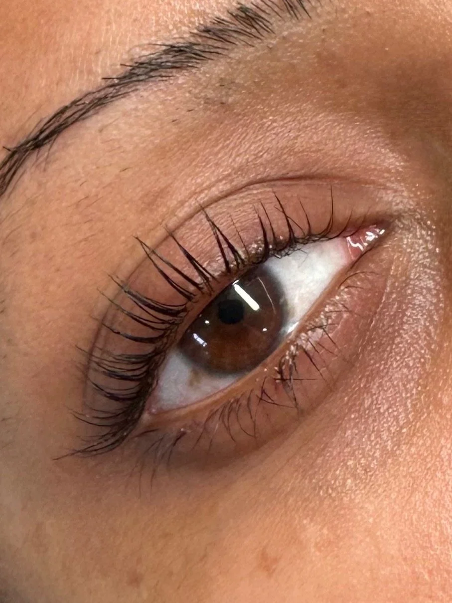Close-up of a human eye with brown iris, long eyelashes, and visible skin texture surrounding the eye.