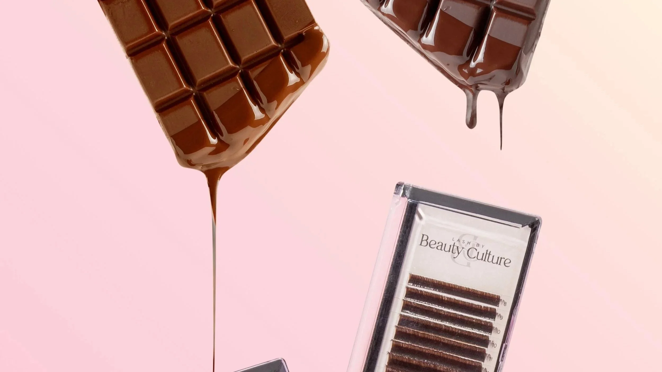 Two pieces of chocolate dripping with melted chocolate and a set of eyelash extensions in a clear plastic case on a light pink background.