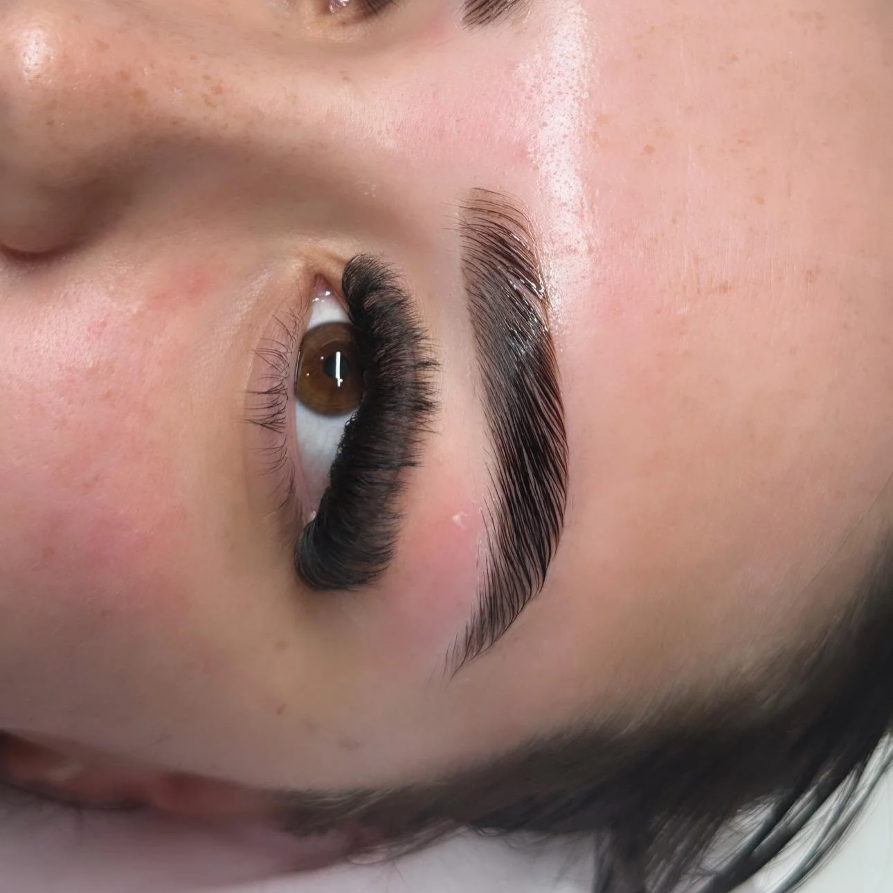 Close-up of a person's face focusing on eye makeup and false eyelashes applied on one eye, with natural skin texture and light makeup.