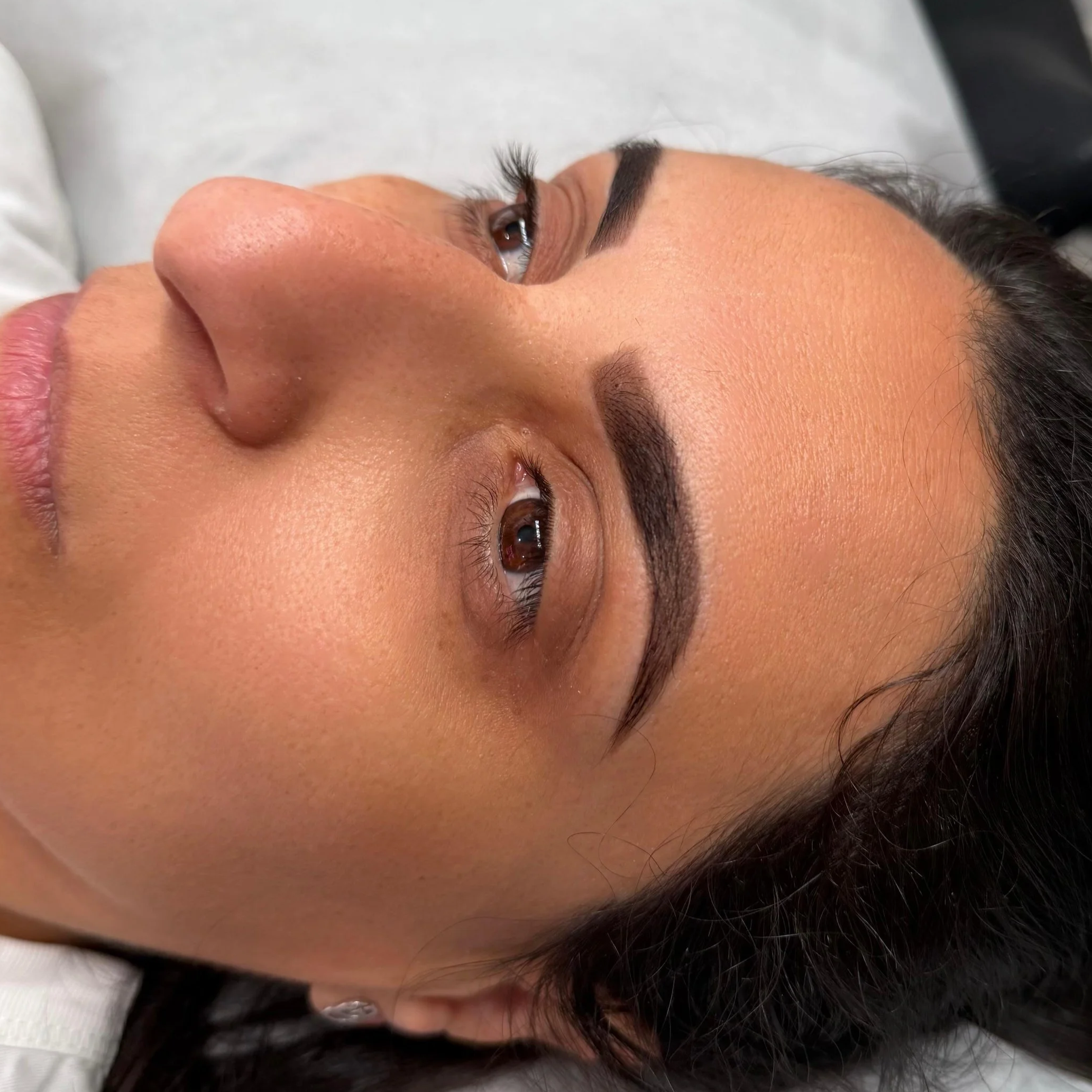 Close-up of a woman's face with well-groomed eyebrows and makeup, lying down and looking up.