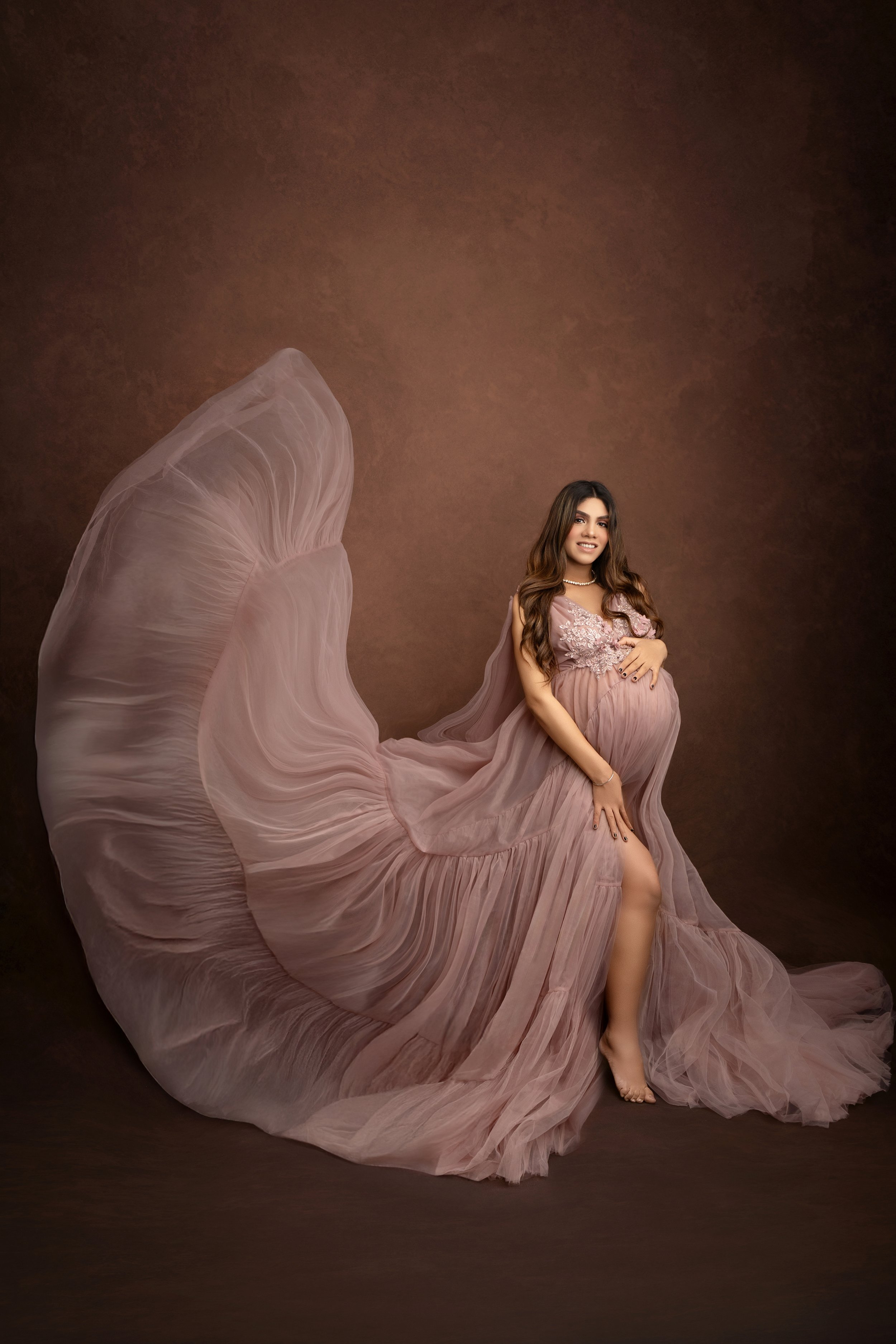Pregnant woman in a flowing pink gown with a textured brown background