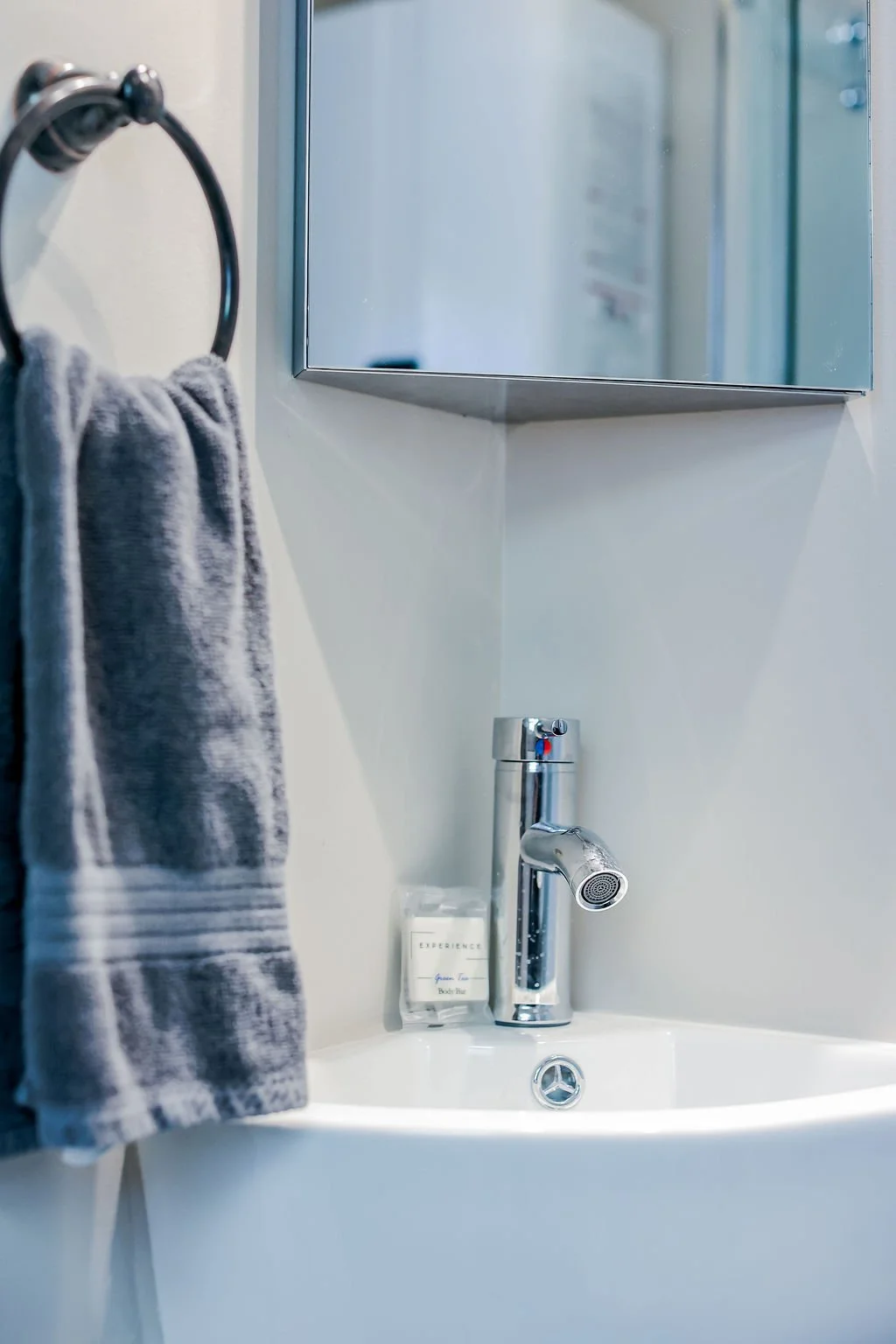 A bathroom sink with a chrome faucet, a soap bar, a gray towel hanging on a towel ring, and a mirrored cabinet above the sink.